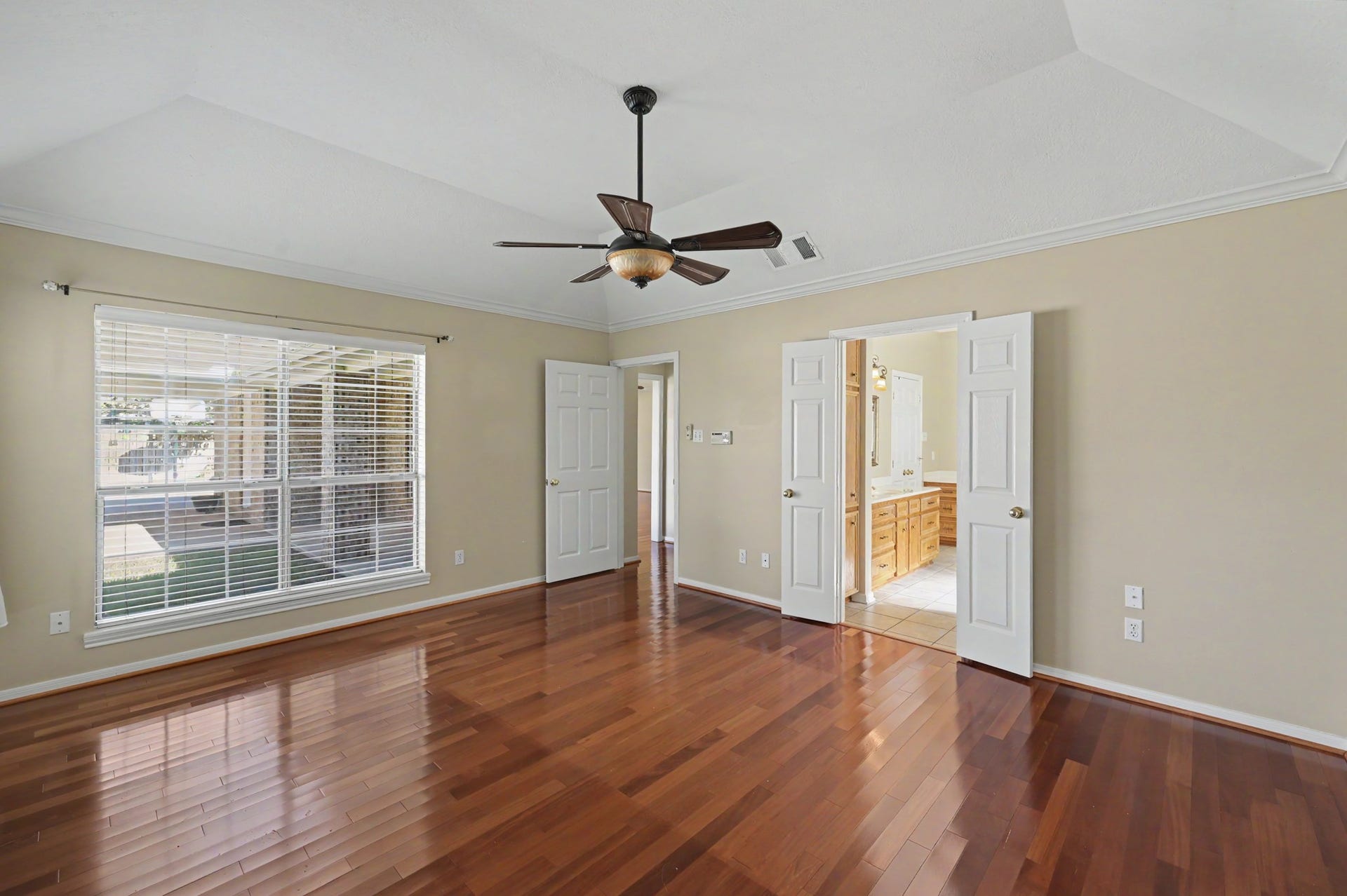 419 Dover Lane, Spring, TX 77373 Another view of primary bedroom with gleaming hardwood floors, large windows streaming with natural light. Double doors lead to an en-suite bathroom, enhancing both style and convenience.