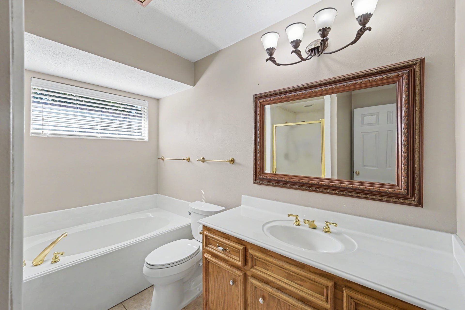 419 Dover Lane, Spring, TX 77373 Guest bathroom featuring a spacious bathtub, separate shower, a vanity with gold fixtures, and a large framed mirror, complemented by natural light from the window.