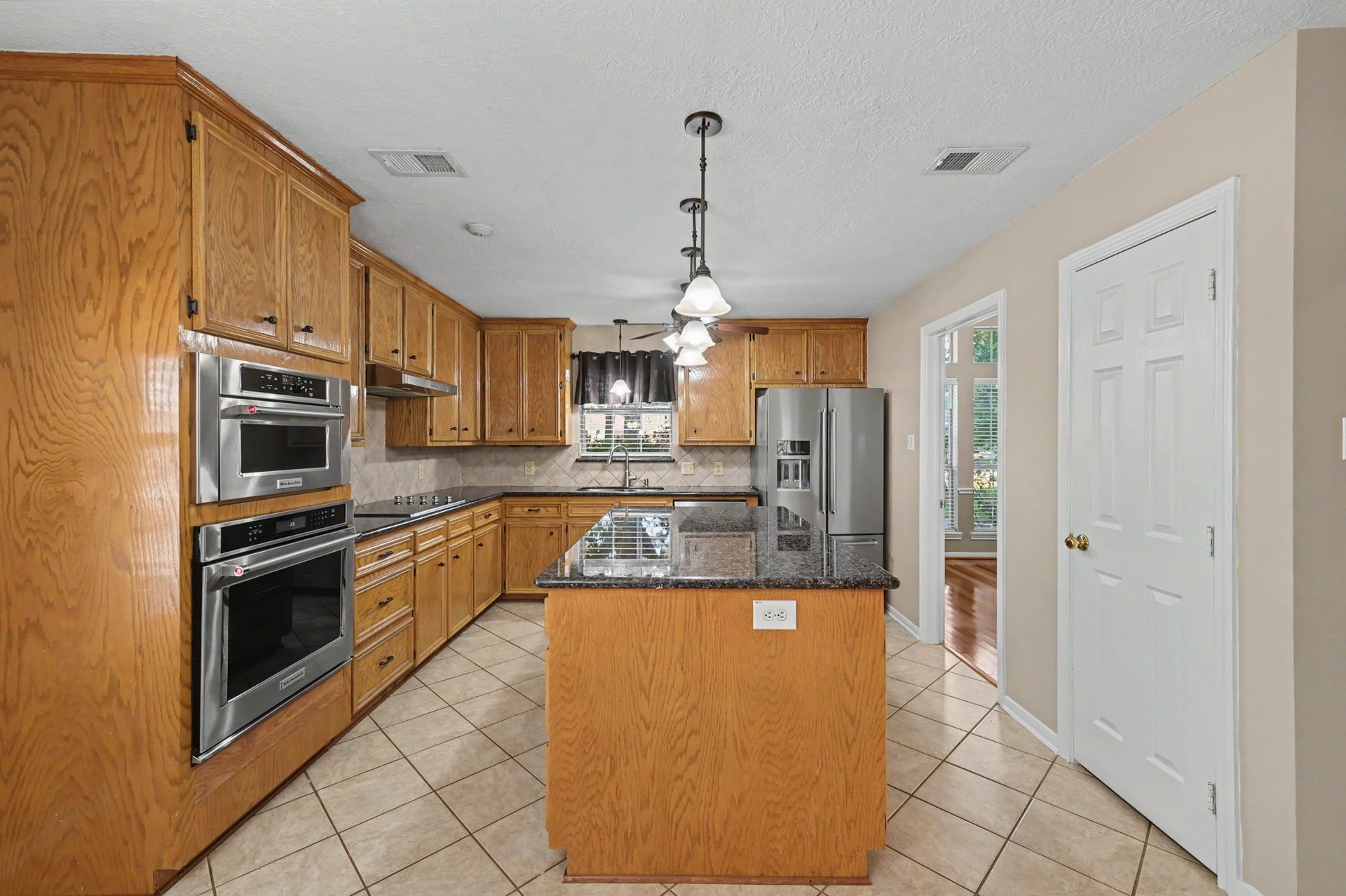 419 Dover Lane, Spring, TX 77373 Spacious kitchen with warm wood cabinetry, granite countertops, and sleek stainless steel appliances, featuring a central island and elegant pendant lighting.
