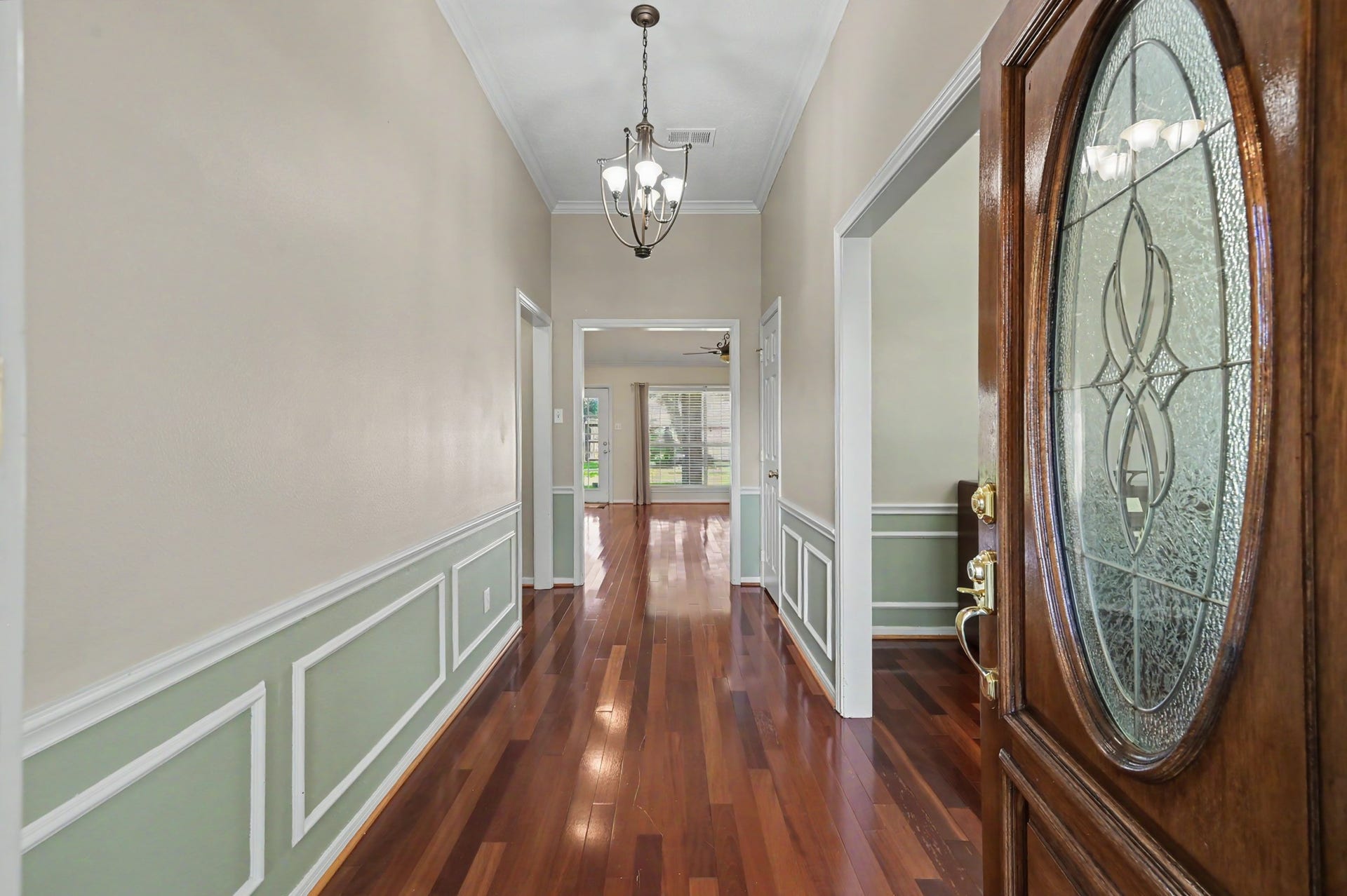 419 Dover Lane, Spring, TX 77373 Elegant entryway featuring rich wood flooring, decorative wainscoting, and a striking glass-paneled front door, leading to a bright and inviting interior. Formal dining room on the right of the entryway.