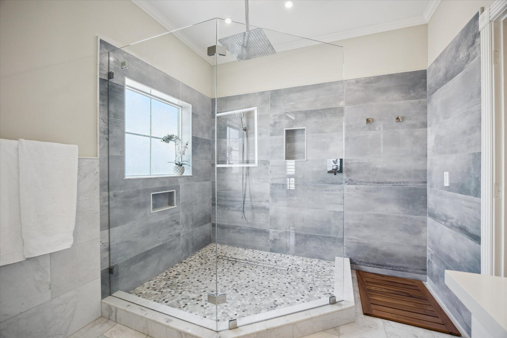5717 Val Verde Street, #C, Houston, TX 77057 This spacious bathroom features a modern, glass-enclosed shower with elegant gray tiles and a pebble stone floor. It includes built-in niches for storage and a rain shower head for a luxurious experience.