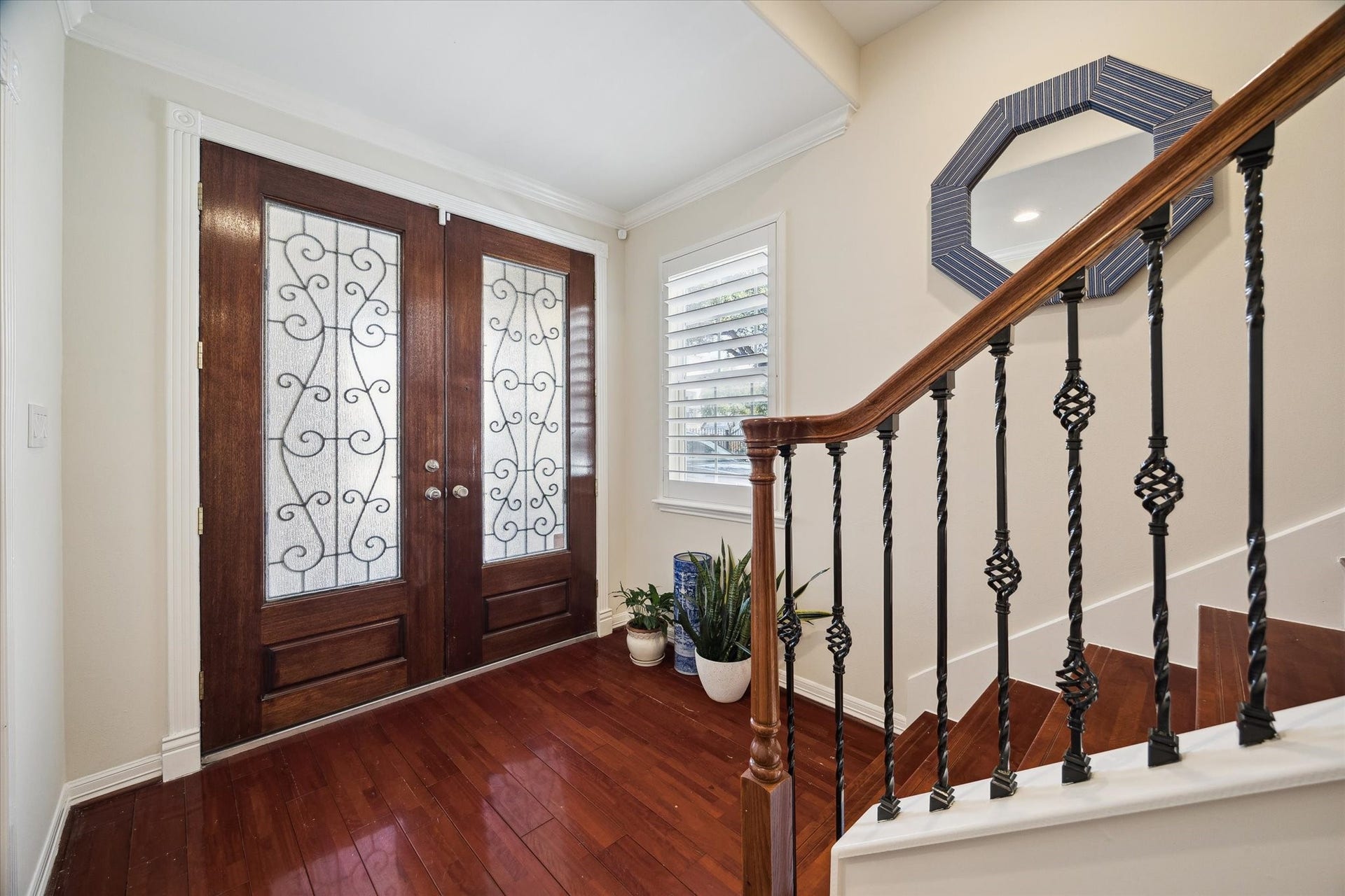 5717 Val Verde Street, #C, Houston, TX 77057 This inviting entryway features elegant double wooden doors with decorative glass and ironwork. It has rich hardwood floors and a stylish staircase with wrought iron balusters. A window with plantation shutters adds natural light.