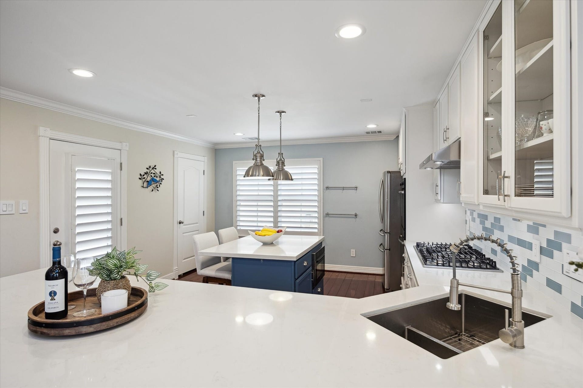 5717 Val Verde Street, #C, Houston, TX 77057 The kitchen features a bright, open layout with white cabinetry, a mosaic backsplash, and a sleek island with bar seating. Stainless steel appliances and ample counter space provide functionality, while pendant lighting and plantation shutters add a stylish touch.