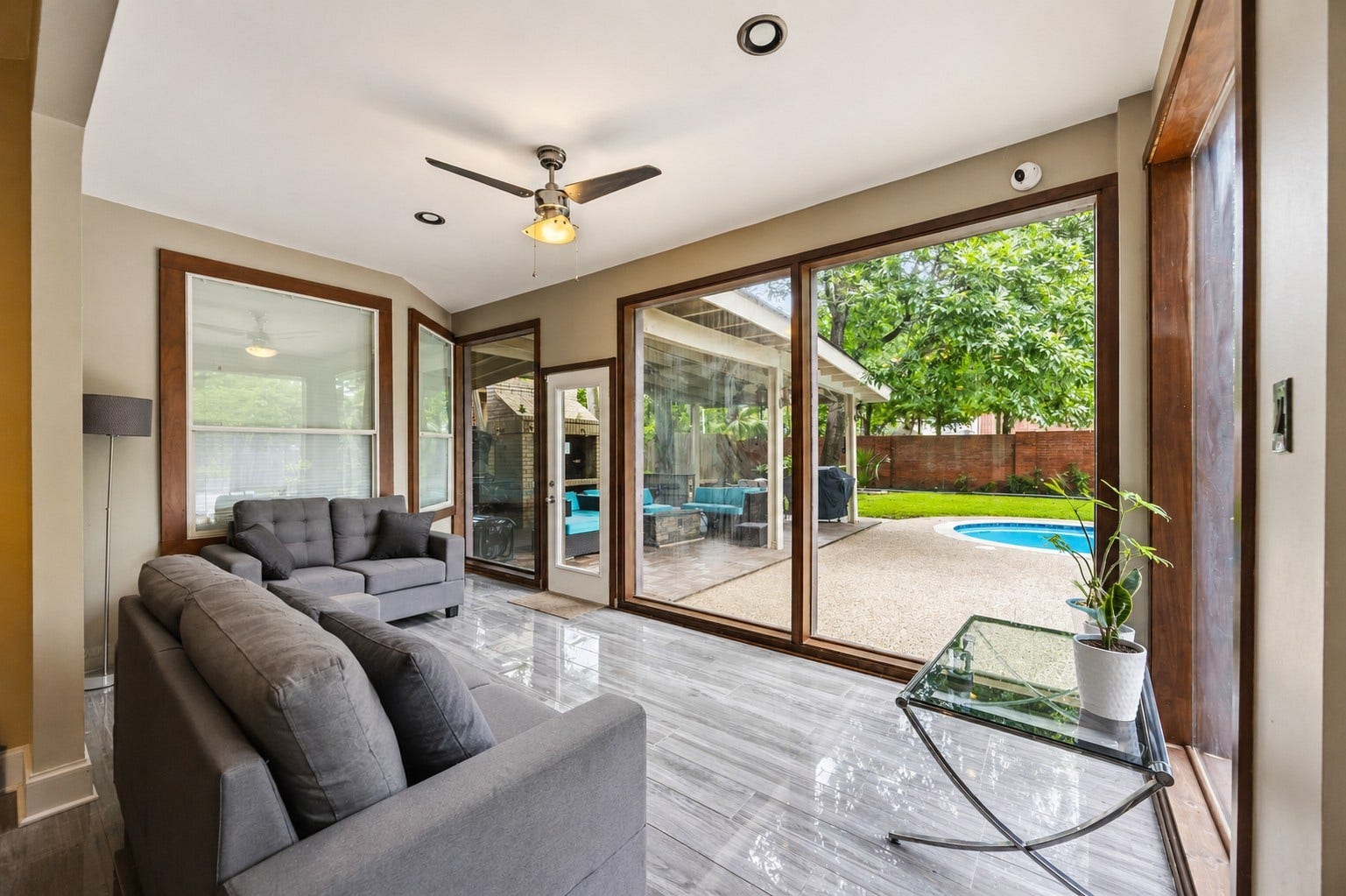 7610 Guinevere Drive, Sugar Land, TX 77479 The bright sunroom boasts large wood-framed windows, a ceiling fan, and glossy wood-look tile floors that overlook the pool area.
