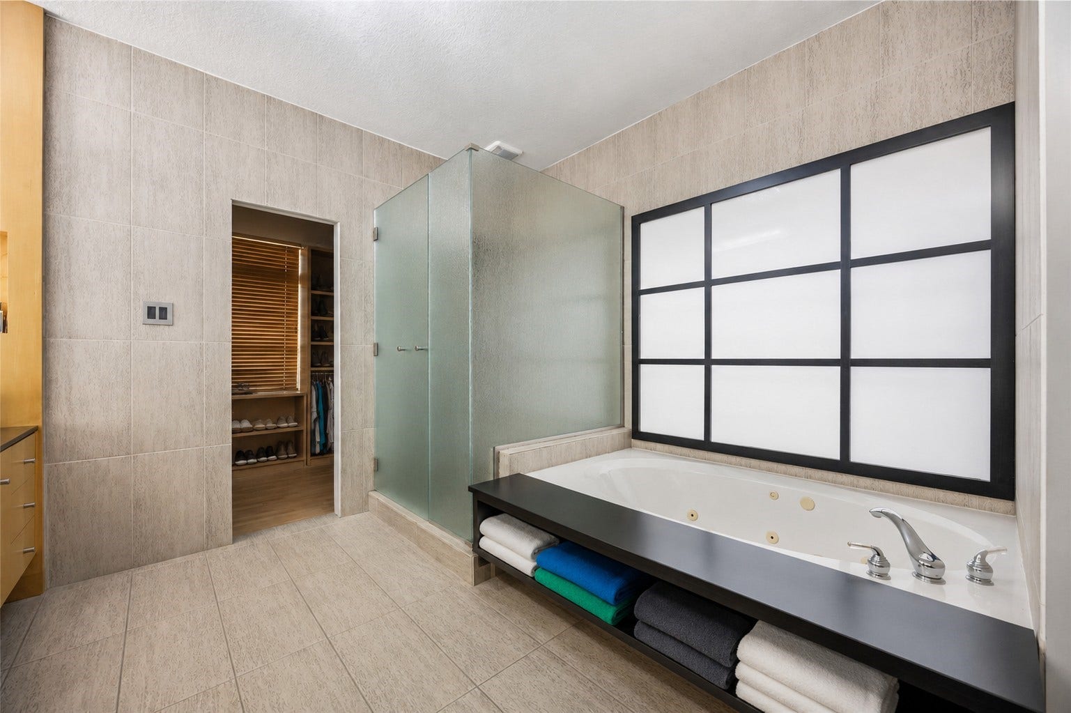 7610 Guinevere Drive, Sugar Land, TX 77479 The spa-like bath area includes a glass-enclosed walk-in shower, tile flooring, and a deep soaking tub set against a large grid-patterned privacy window.