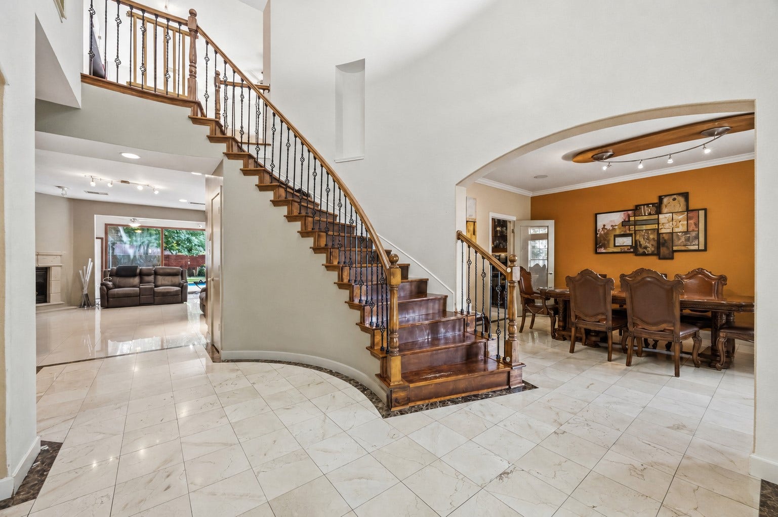 7610 Guinevere Drive, Sugar Land, TX 77479 The bright entryway showcases polished tile flooring with a dark border inlay, a sweeping wooden staircase with wrought-iron spindles, and an arched transition into the adjacent dining area.