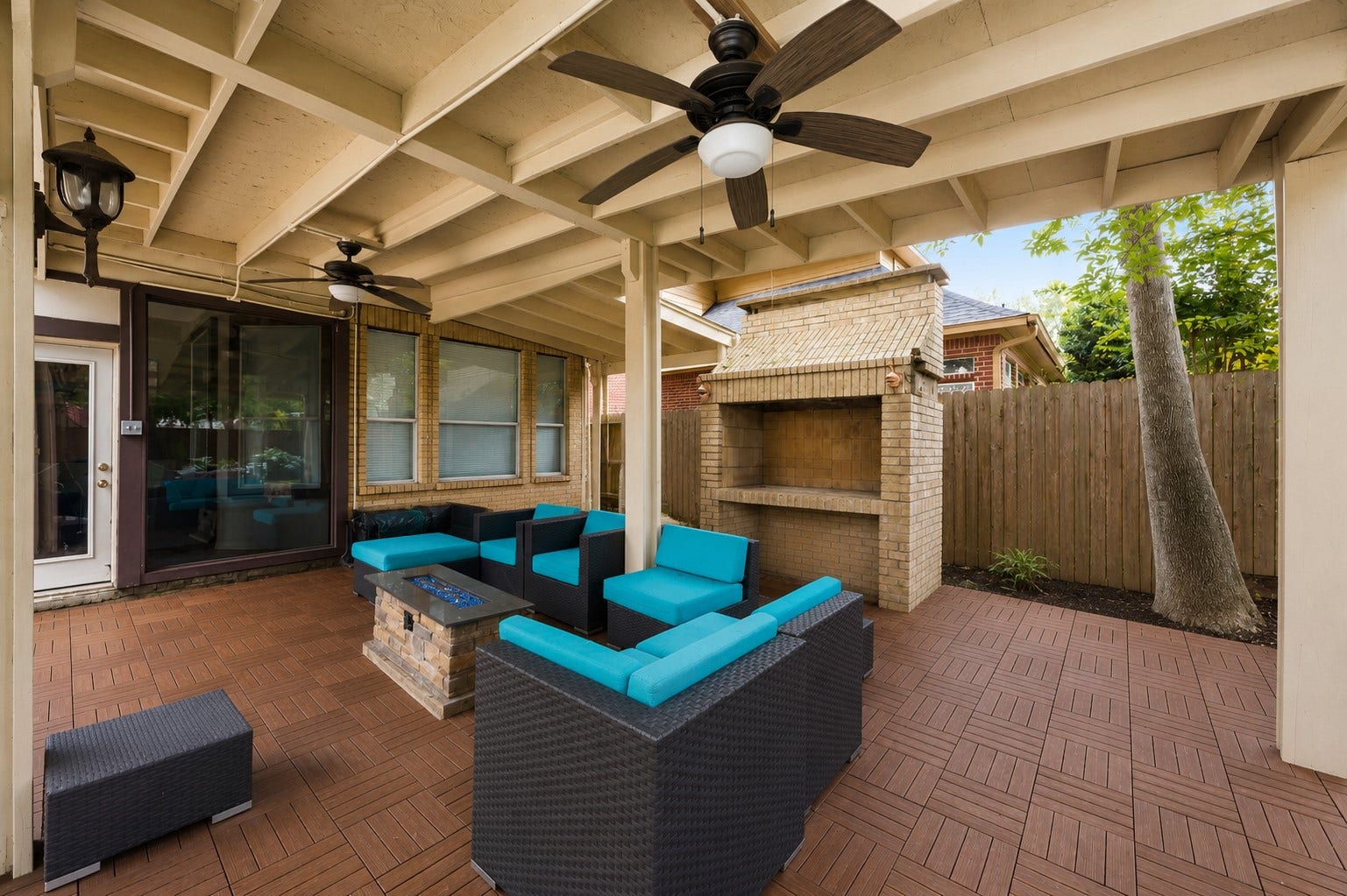 7610 Guinevere Drive, Sugar Land, TX 77479 The covered veranda boasts a rustic exposed-joist ceiling with cooling fans, patterned interlocking deck tiles, and a large built-in brick outdoor fireplace kitchen.
