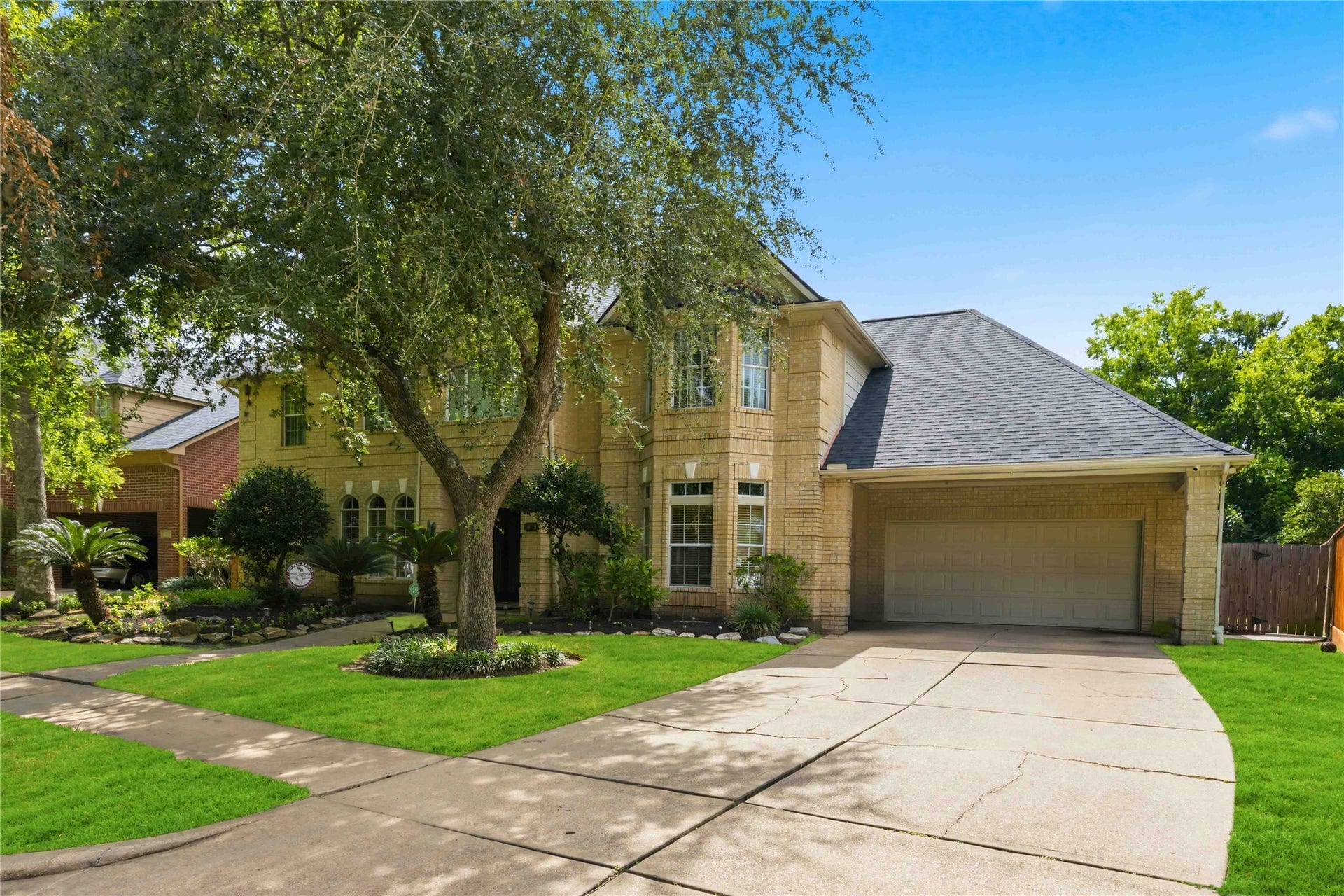 7610 Guinevere Drive, Sugar Land, TX 77479 A wide concrete driveway leads up to an attached two-car garage, showcasing the home's multi-gabled roofline and manicured front lawn.