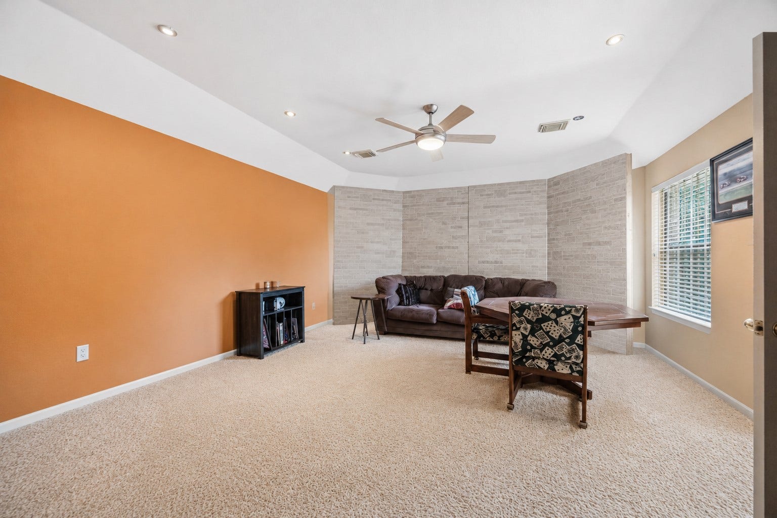 7610 Guinevere Drive, Sugar Land, TX 77479 This expansive upstairs bedroom features plush beige carpeting, a central ceiling fan, an orange accent wall, and a unique textured brick-look focal wall.