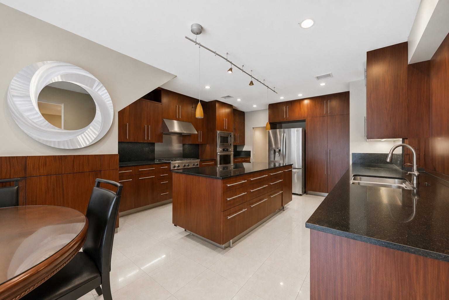 7610 Guinevere Drive, Sugar Land, TX 77479 The contemporary kitchen showcases rich wood cabinetry, dark granite countertops, and an expansive central island lit by track lighting.