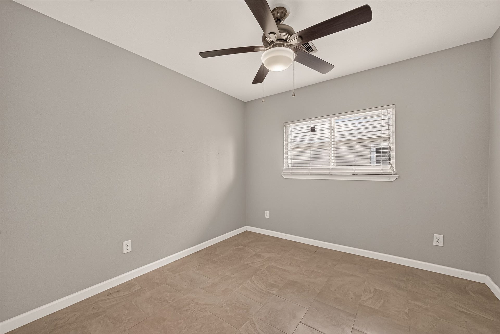 Bright and cozy, this versatile room features neutral gray walls, tile flooring, and a modern ceiling fan, ideal for a bedroom or home office.