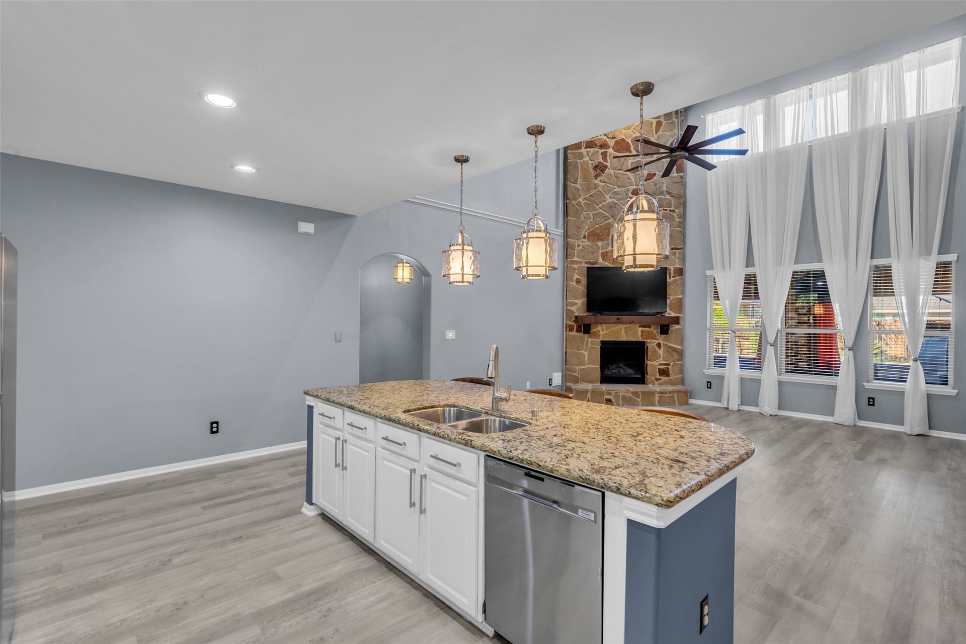 8121 Tranquil Lake Way, Conroe, TX 77385 Spacious living area featuring a stunning stone fireplace, high ceilings with elegant drapery, and a modern kitchen island with granite countertops and pendant lighting.