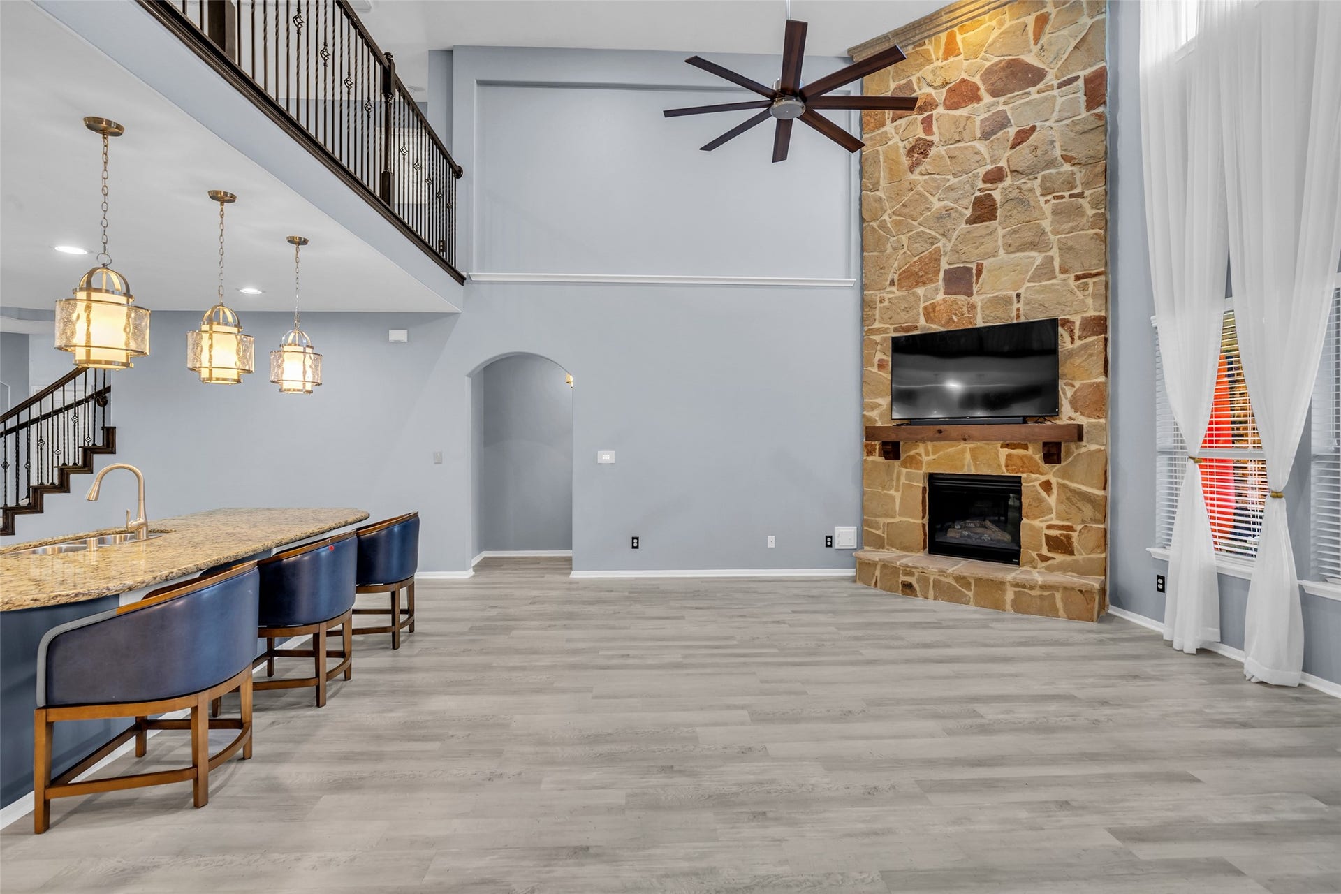 8121 Tranquil Lake Way, Conroe, TX 77385 Spacious living area with a stunning stone fireplace, modern ceiling fan, and large windows that fill the room with natural light. The open layout includes a sleek kitchen island with elegant pendant lighting and bar seating, perfect for entertaining.