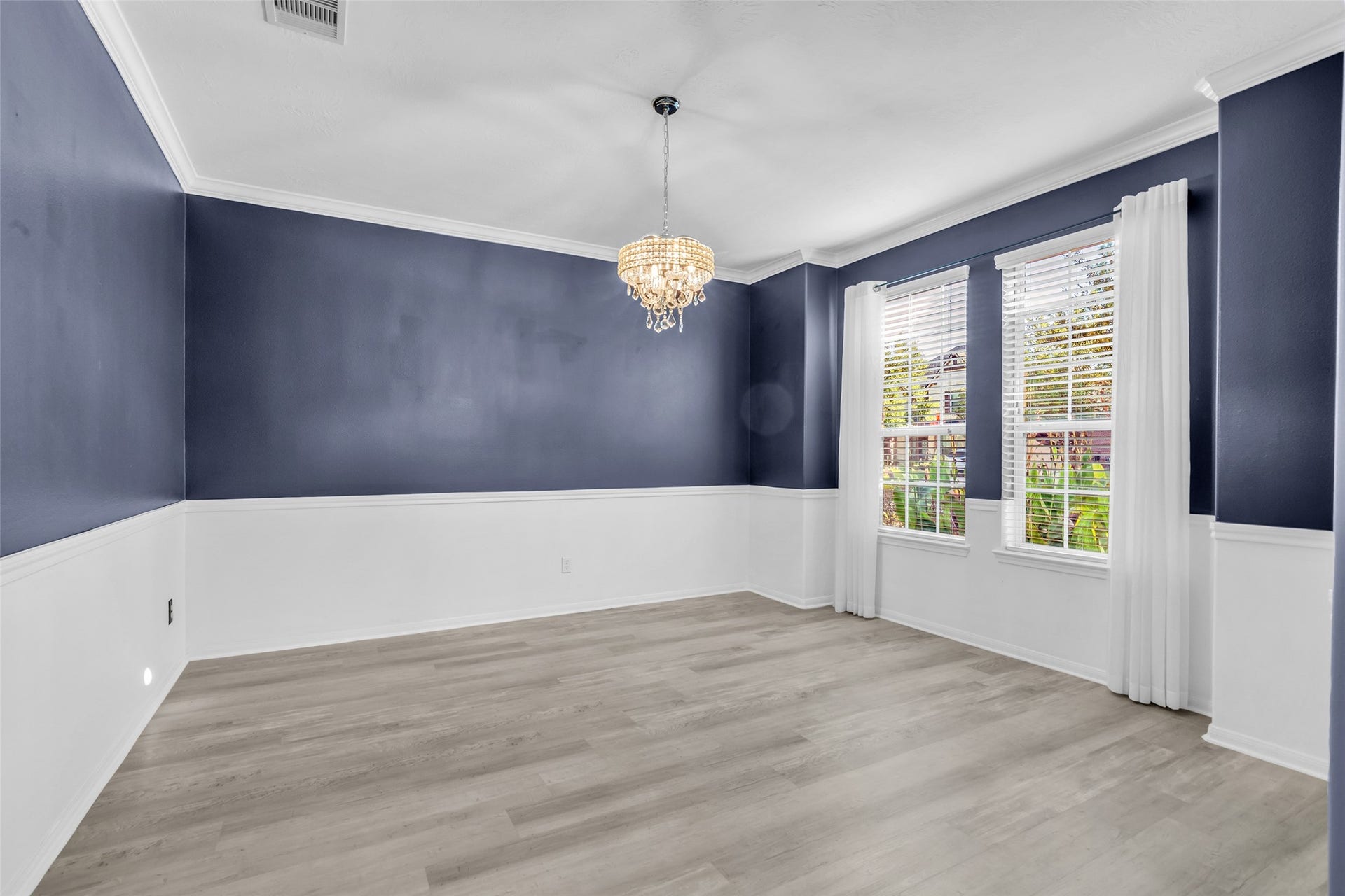8121 Tranquil Lake Way, Conroe, TX 77385 Elegant formal dining room featuring rich blue walls with white wainscoting, accented by a classic chandelier and large windows that fill the space with natural light.