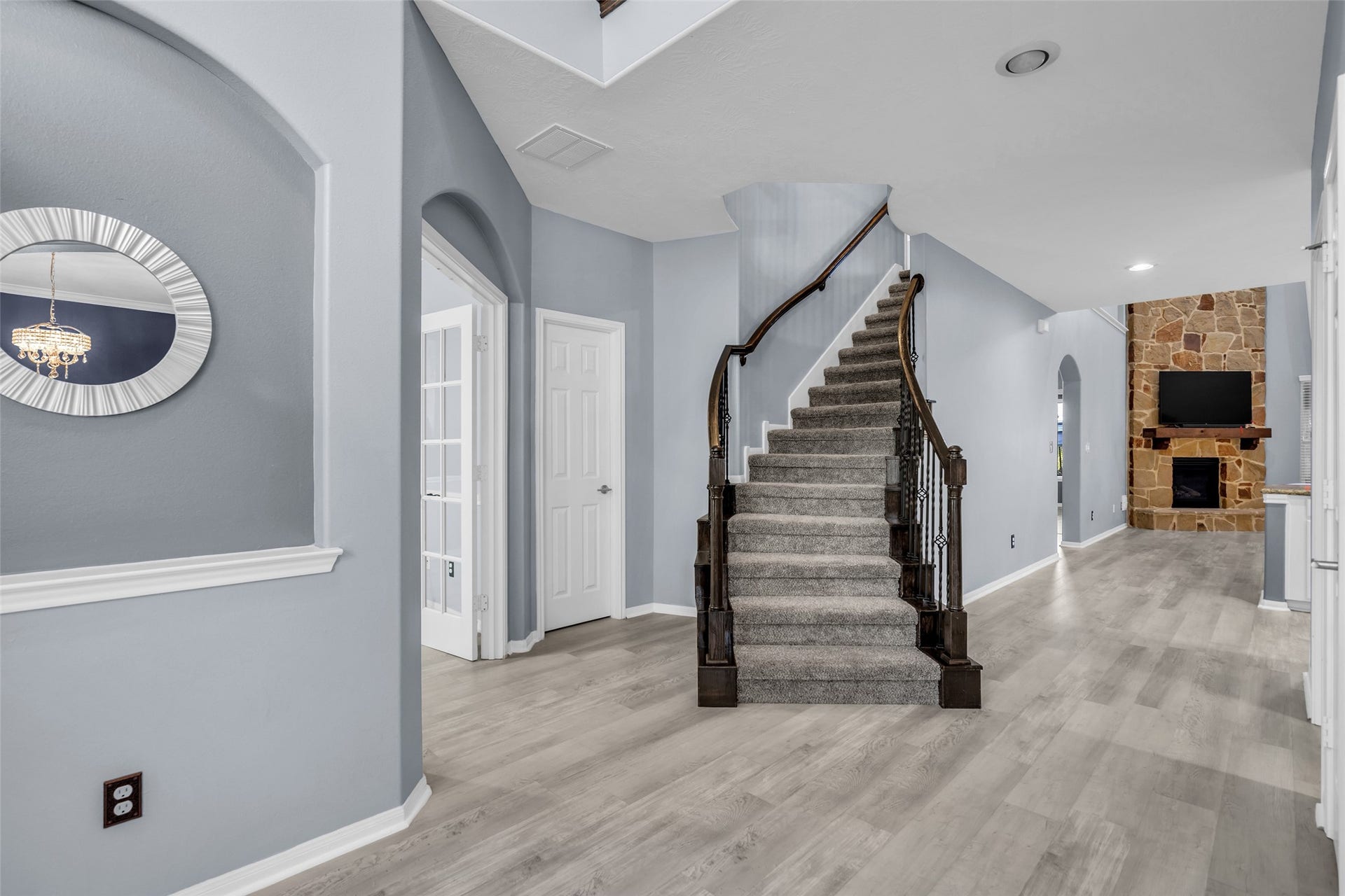 8121 Tranquil Lake Way, Conroe, TX 77385 Elegant entryway featuring a graceful curved staircase, modern gray flooring, and a cozy stone fireplace in the living area.