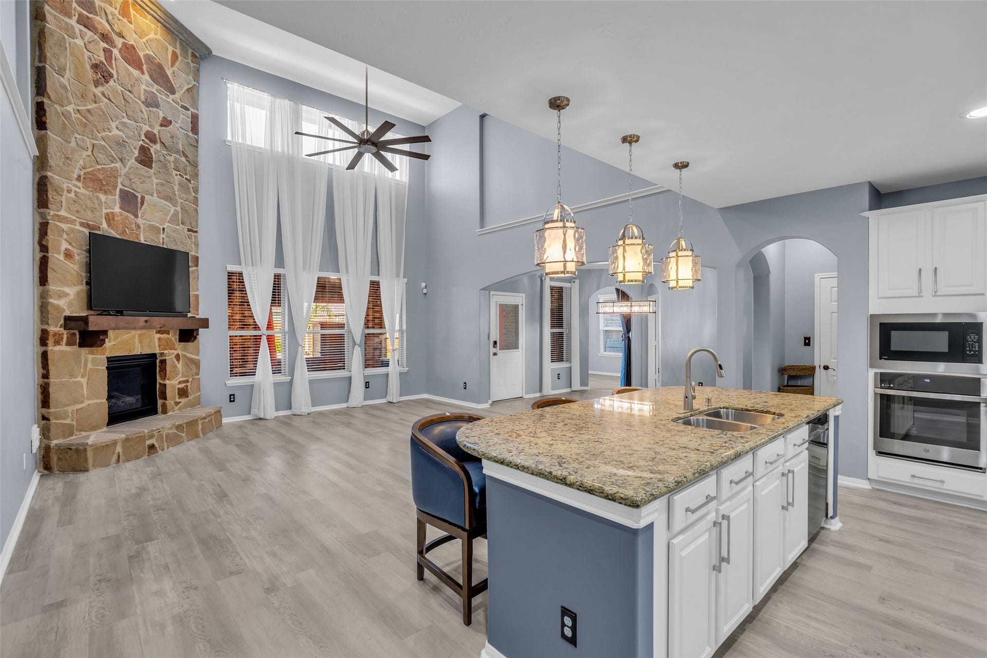 8121 Tranquil Lake Way, Conroe, TX 77385 Spacious open-concept living area featuring a stunning stone fireplace, high ceilings with a modern fan, and a gourmet kitchen with granite countertops and elegant pendant lighting.
