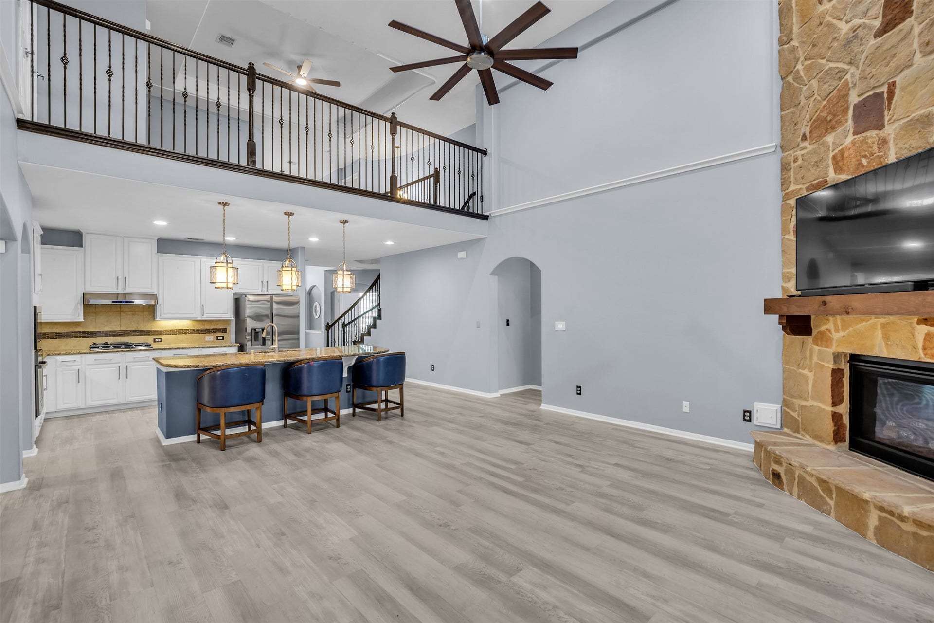 8121 Tranquil Lake Way, Conroe, TX 77385 Spacious open-concept living area featuring a vaulted ceiling, elegant stone fireplace, and modern kitchen with an island bar. The loft-style railing adds a touch of sophistication, complemented by sleek wood flooring and ample natural light.