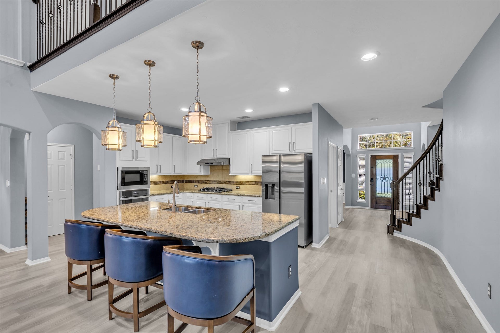 8121 Tranquil Lake Way, Conroe, TX 77385 Elegant kitchen with a spacious granite island, modern stainless steel appliances, and stylish pendant lighting, seamlessly connecting to an inviting entryway and curved staircase.