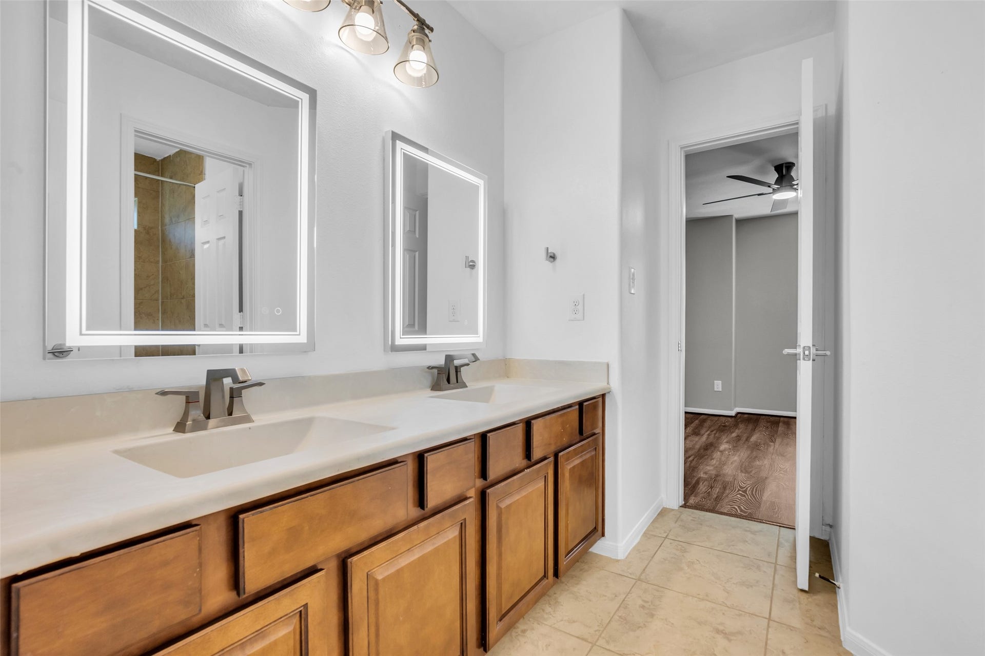 8121 Tranquil Lake Way, Conroe, TX 77385 Upstairs secondary jack and jill bathroom featuring a double vanity with illuminated mirrors and stylish fixtures, complemented by warm wood cabinetry and sleek tiling.