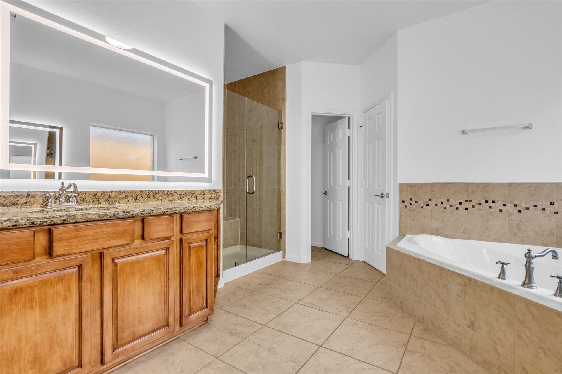8121 Tranquil Lake Way, Conroe, TX 77385 Spacious bathroom featuring a granite-topped vanity with ample storage, a luxurious soaking tub, and a modern glass-enclosed shower.