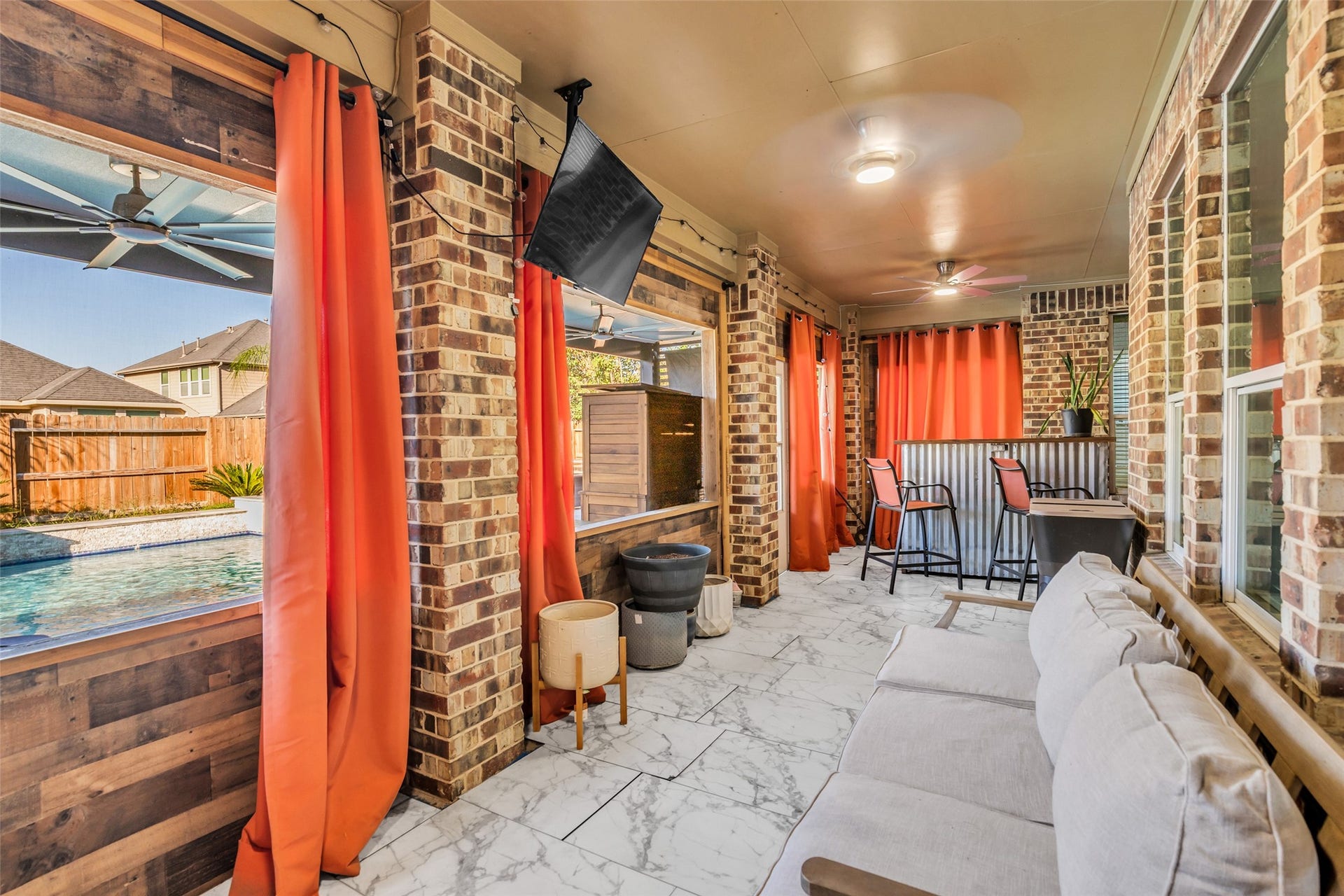 8121 Tranquil Lake Way, Conroe, TX 77385 Charming sunroom with brick accents, vibrant orange curtains, and a view of the pool. Enjoy relaxing on the comfortable seating or entertaining at the bar area.