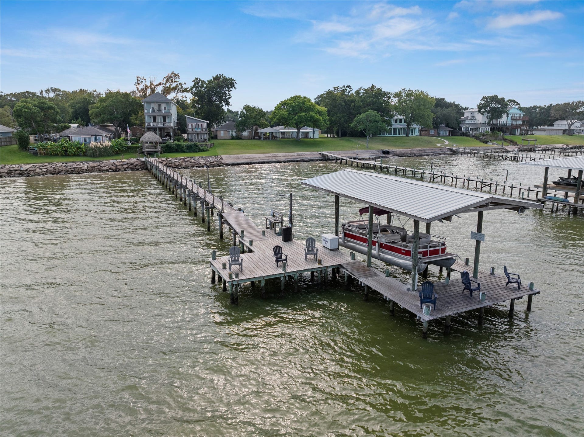 3709 Bayshore Drive, #1-12, Bacliff, TX 77518 This waterfront property features a long pier leading to a spacious dock with seating and a covered boat area, offering serene views and direct access to the water.