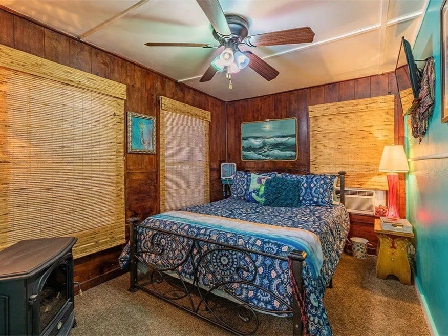 3709 Bayshore Drive, #1-12, Bacliff, TX 77518 Cozy and inviting bedroom in the Saltwater Gypsy with a nautical theme, featuring warm wood paneling, vibrant decor, and a ceiling fan for comfort. Perfect for a tranquil retreat.