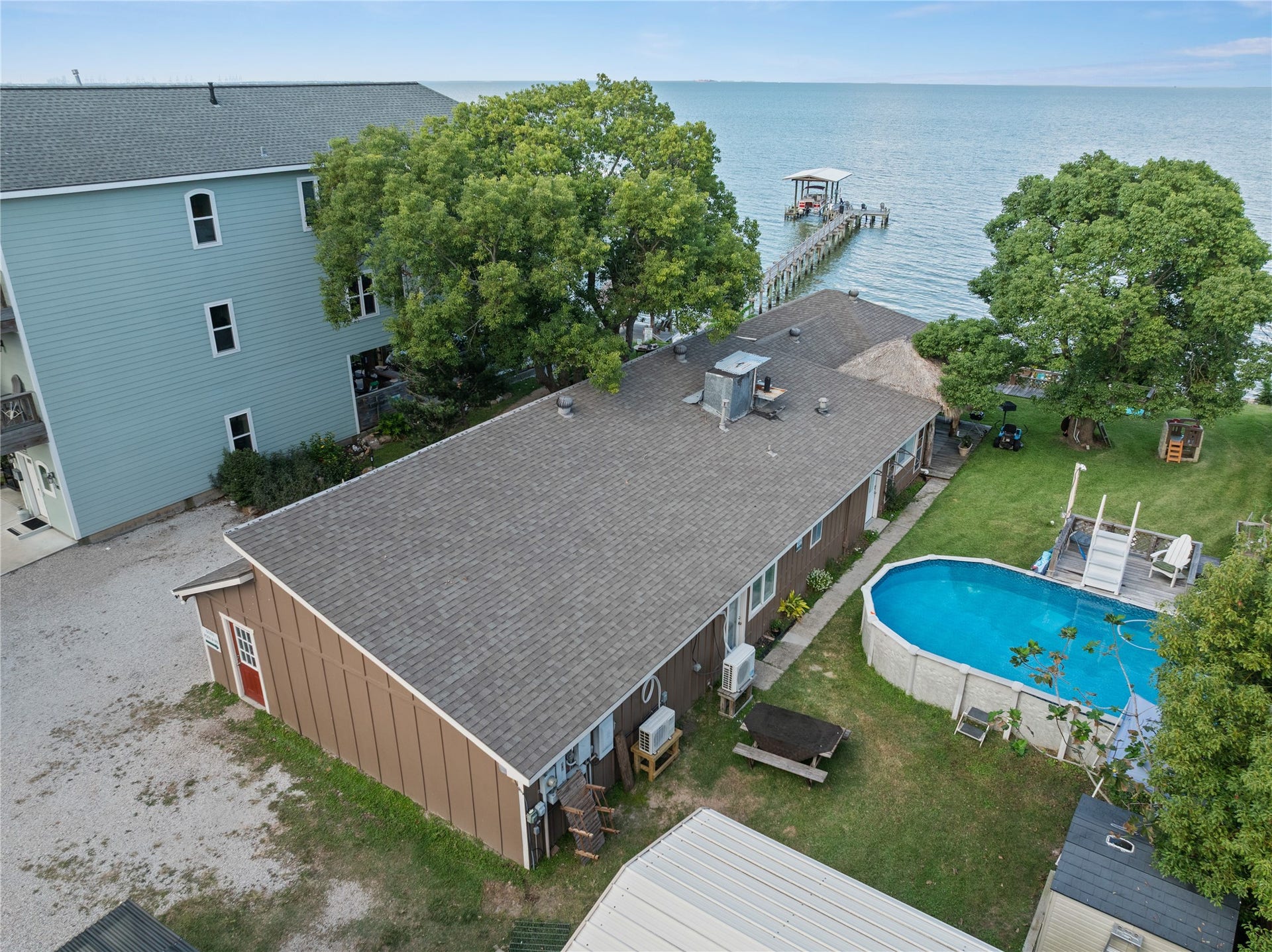 3709 Bayshore Drive, #1-12, Bacliff, TX 77518 This photo features a spacious one-story Ohana House and Bay Room with a large backyard, a wooden dock extending into the water. Surrounded by greenery, it offers serene views and direct access to the water, perfect for those seeking a peaceful retreat.
