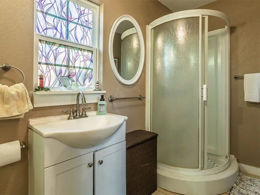 3709 Bayshore Drive, #1-12, Bacliff, TX 77518 Charming bathroom in the Doc Holiday with a stylish round shower, elegant oval mirror, and inviting natural light through decorative windows. Perfect for relaxation.
