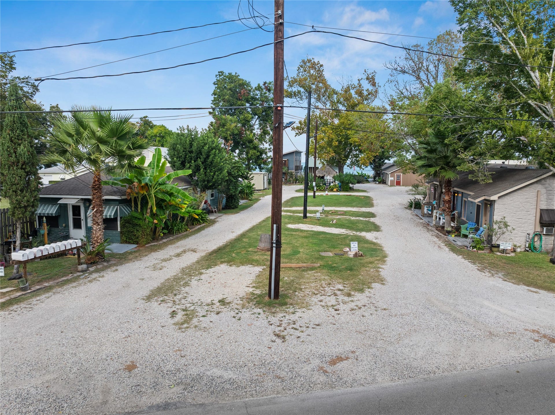 3709 Bayshore Drive, #1-12, Bacliff, TX 77518 This photo shows a quaint property with small homes lining a gravel road. The street is flanked by trees and greenery, creating a cozy atmosphere.