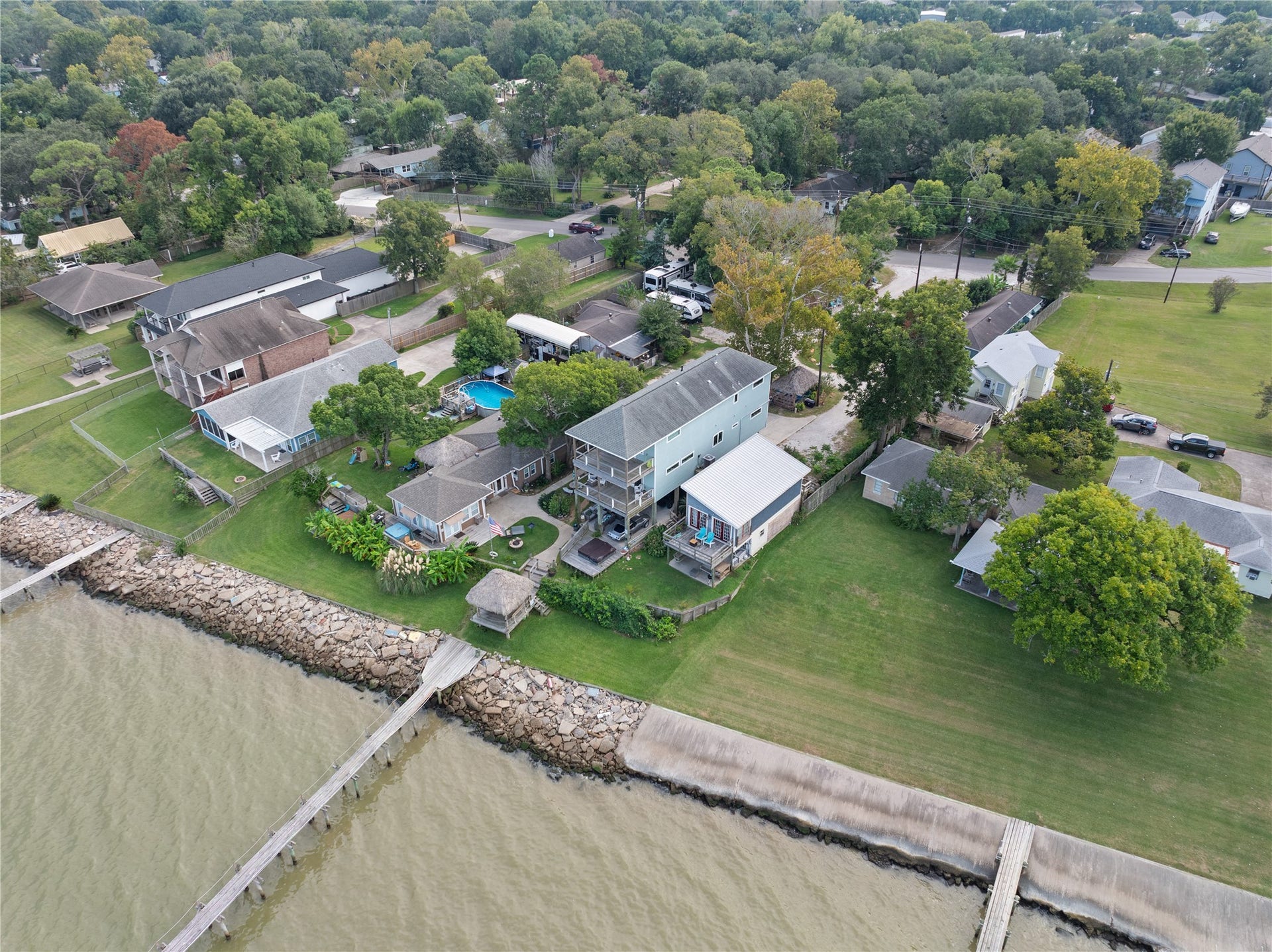 3709 Bayshore Drive, #1-12, Bacliff, TX 77518 This aerial view showcases the charming waterfront property with a spacious backyard and private pier. The neighborhood is lush with trees, offering a serene, natural setting. Nearby homes are well-maintained, and the area provides a sense of community and privacy.