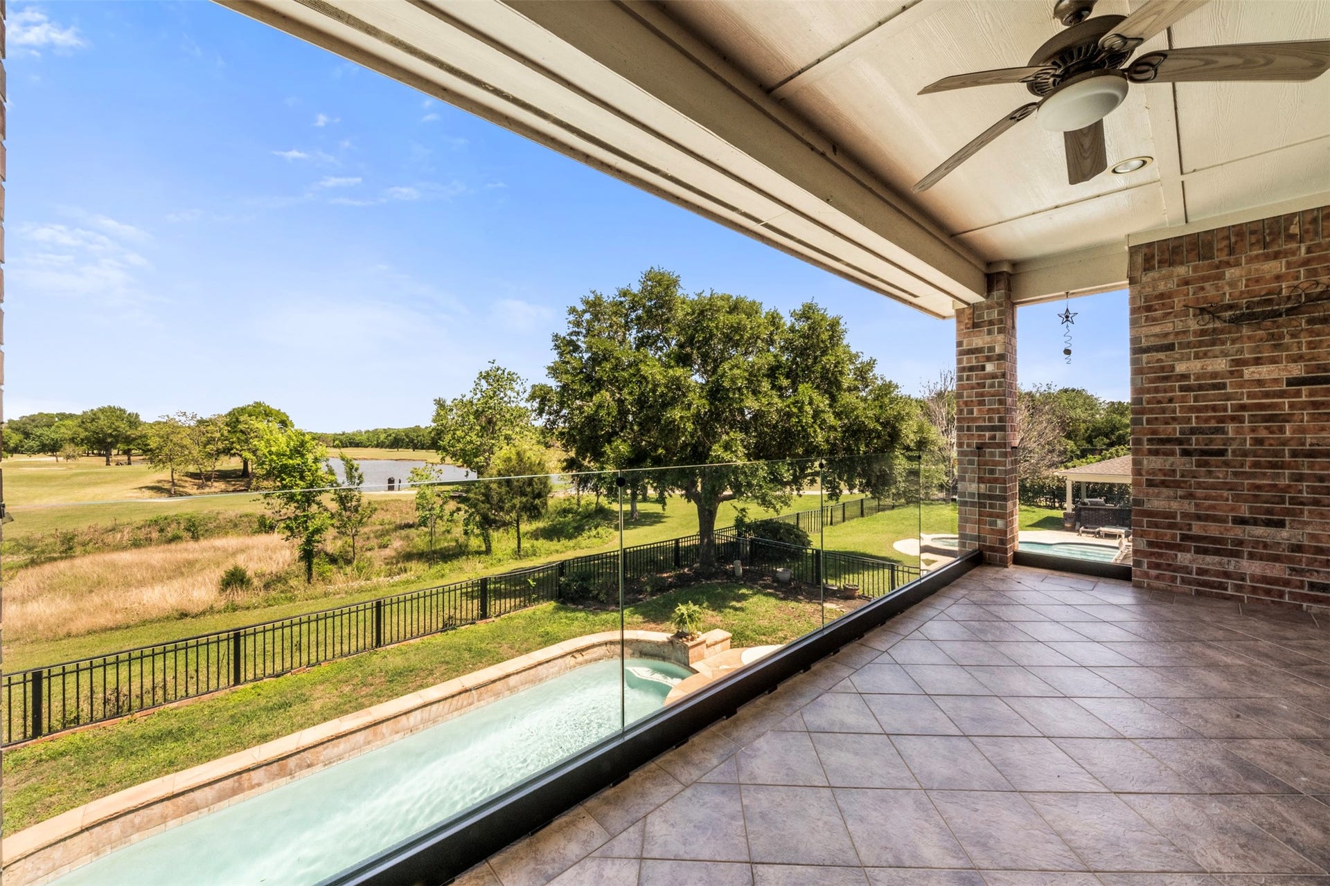 26418 Cottage Cypress Lane, Cypress, TX 77433 A stunning upper-level balcony featuring a glass railing for uninterrupted views, and an incredible vista of the swimming pool, lush greenbelt, and a serene lake. Right outside the large gameroom.