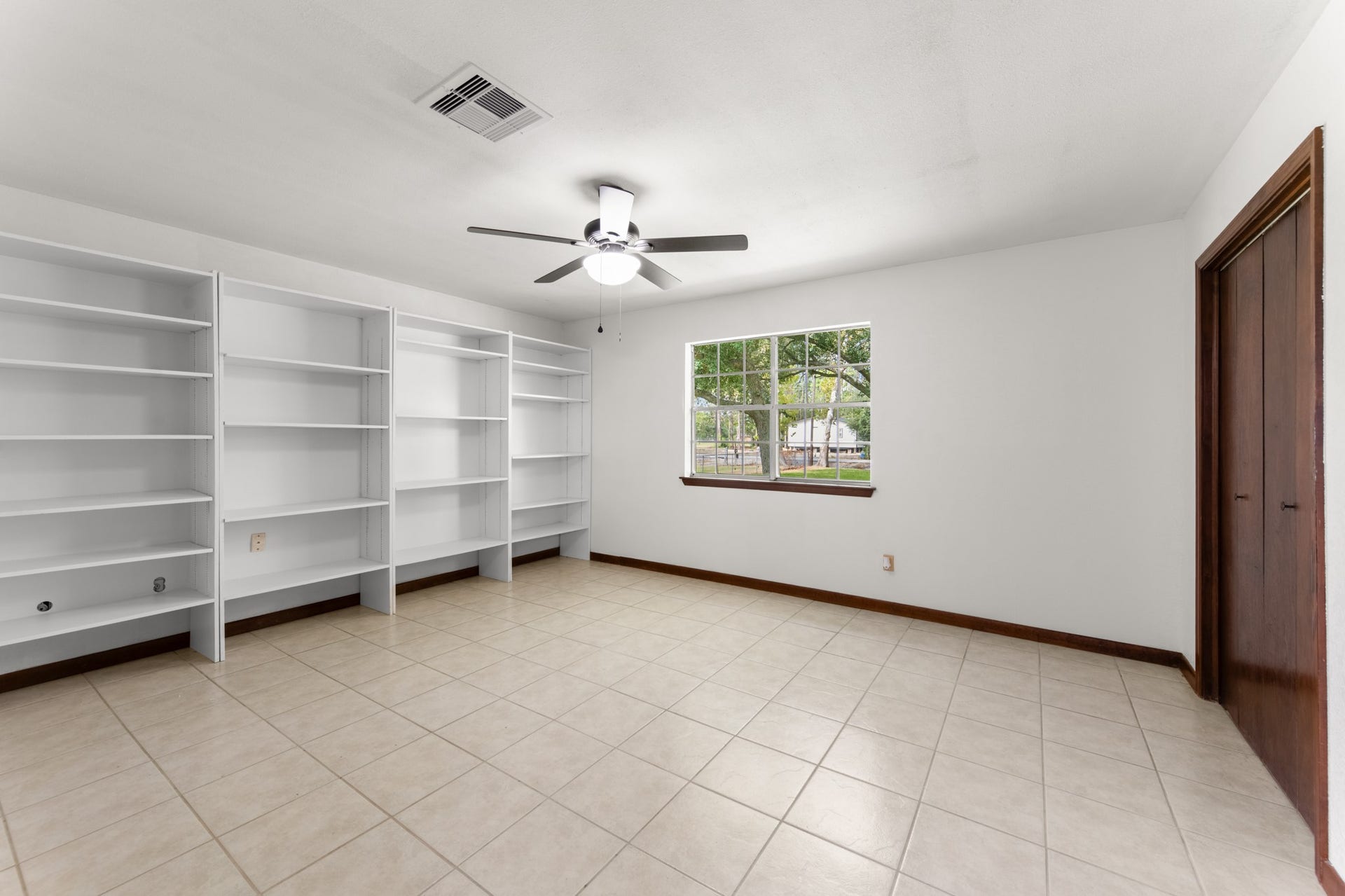 11325 32nd Street, Santa Fe, TX 77510 Spacious primary bedroom featuring a wall of removable shelving, tile flooring, and a large window overlooking the property grounds.