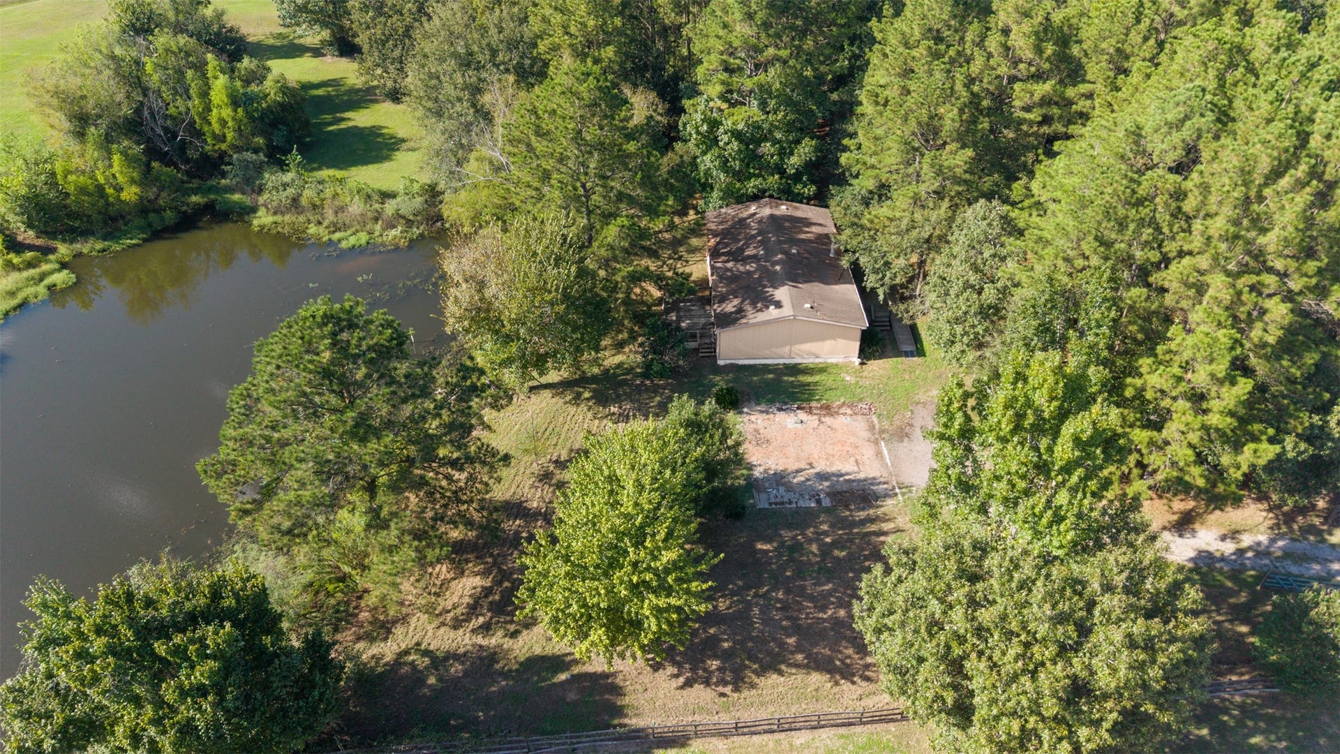 9944 Chestnut Court, Montgomery, TX 77316 An aerial view showcases the property's beautiful natural setting with mature trees, open yard space, and a peaceful pond alongside the home. A wonderful opportunity to enjoy country living surrounded by nature.