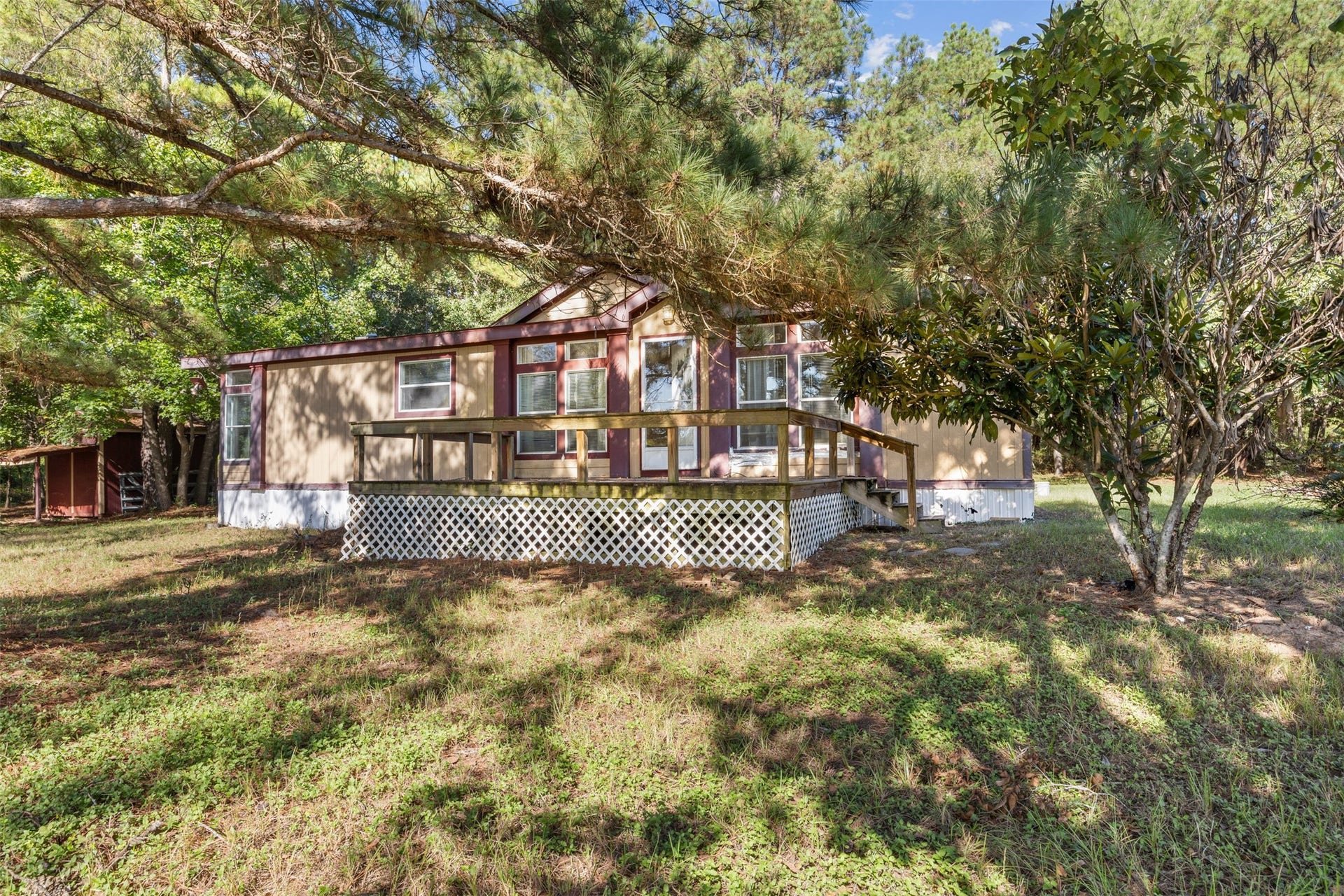 9944 Chestnut Court, Montgomery, TX 77316 A view of the home's rear exterior highlights the spacious wooden deck overlooking the shared pond, with mature trees providing shade and a beautiful natural backdrop for outdoor living.