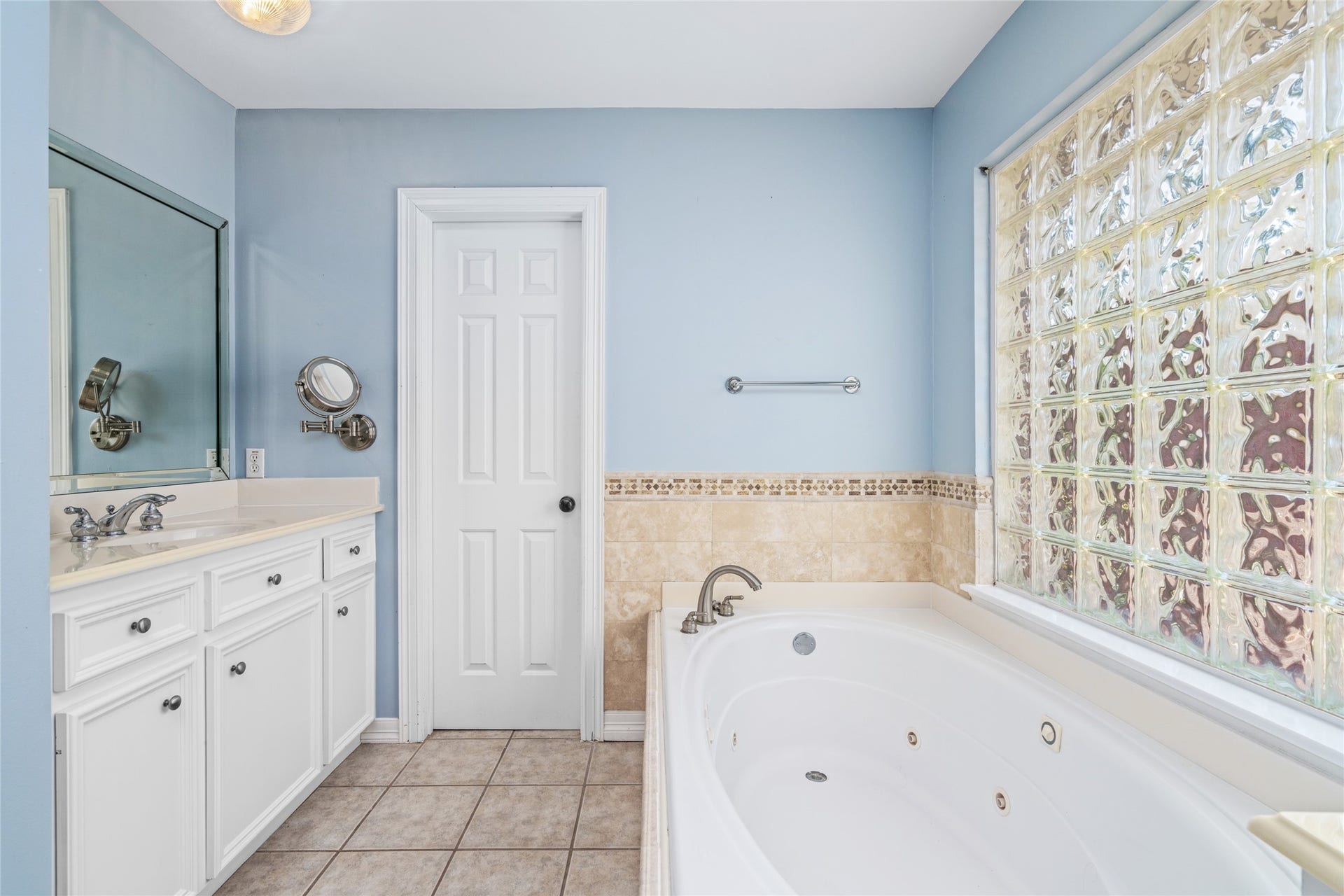 4312 Holt Street, Bellaire, TX 77401 Natural light creates a serene spa-like ambiance over the whirlpool tub. A travertine-style tile surround with an accent mosaic border adds warmth, and the white raised-panel vanity offers generous counter space.