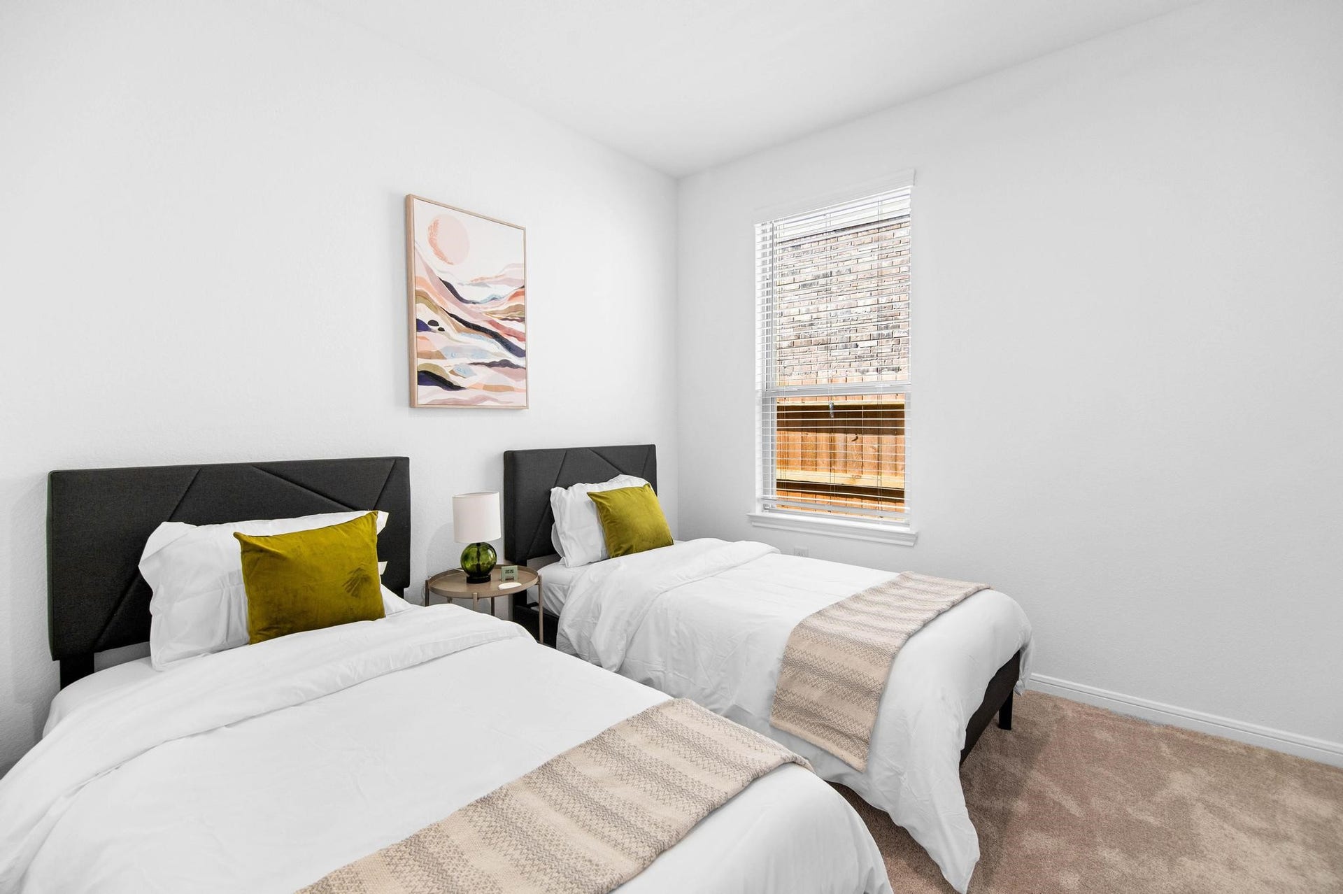 Bright and inviting bedroom with twin beds, plush pillows, and a tasteful piece of art, offering a cozy and comfortable space.