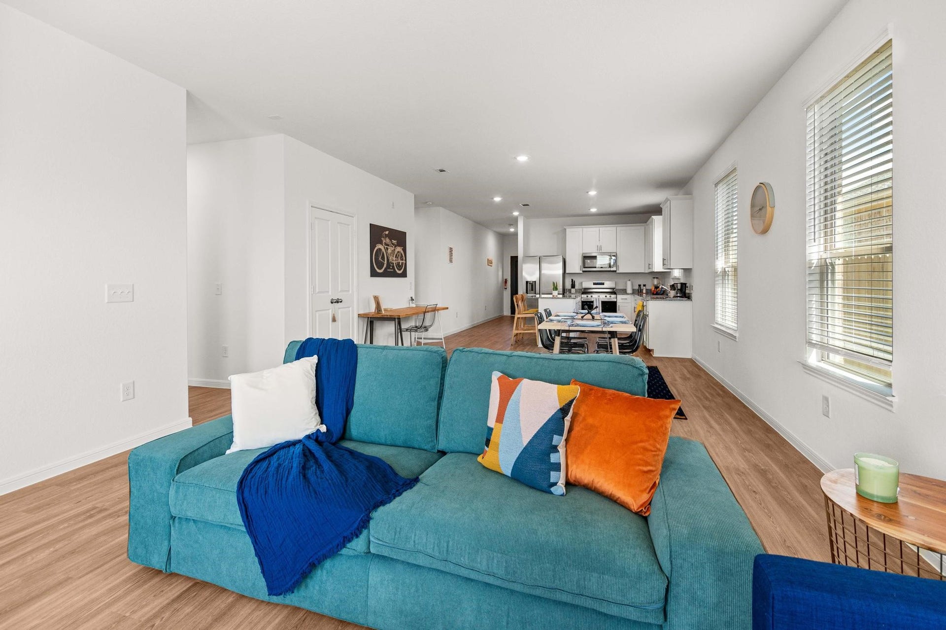 Spacious open-concept living area with modern kitchen, featuring sleek white cabinetry and stainless steel appliances, complemented by warm wood flooring and abundant natural light.