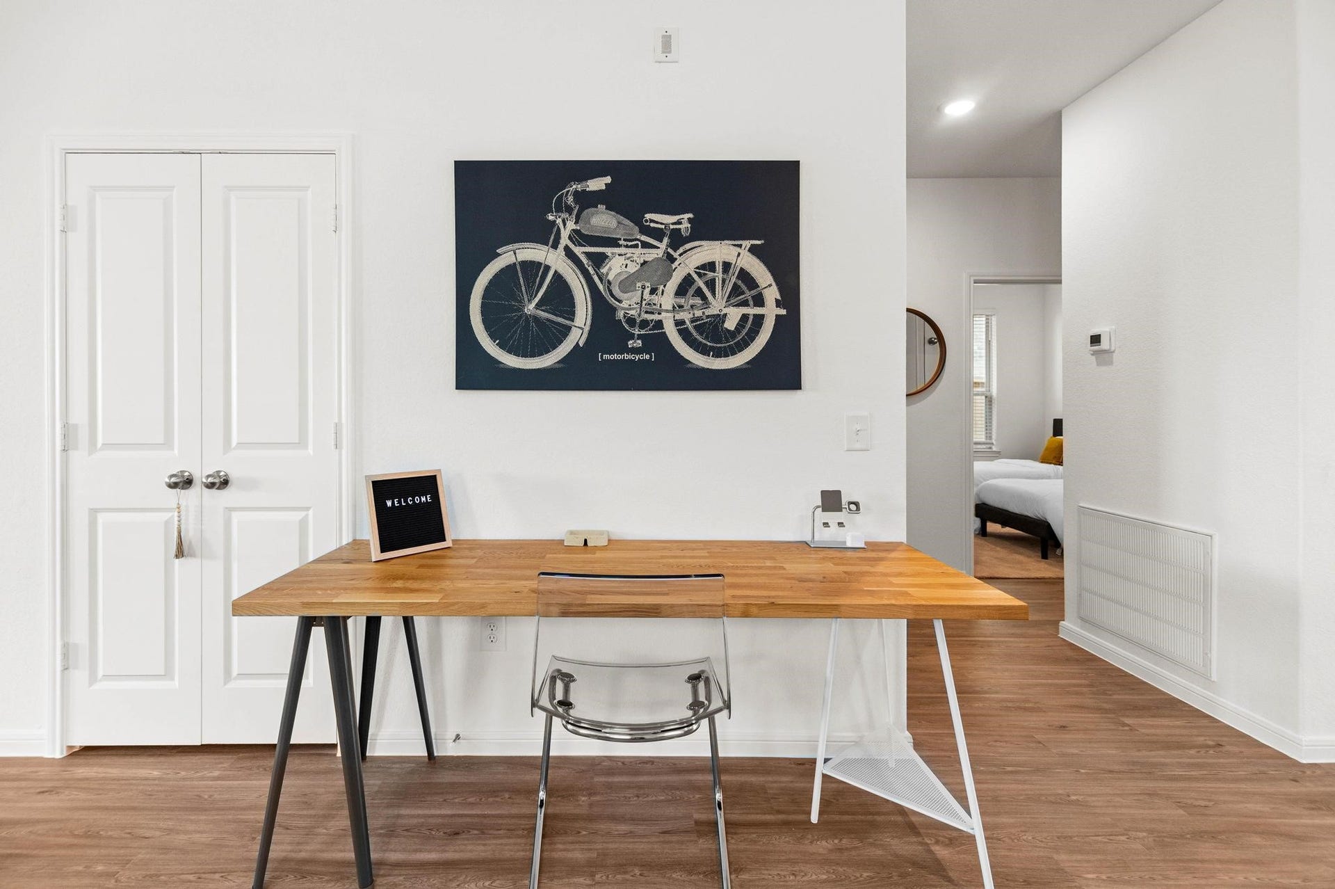 Chic and modern workspace featuring a stylish wooden desk with a clear chair, set against a bright wall adorned with a vintage bicycle print.