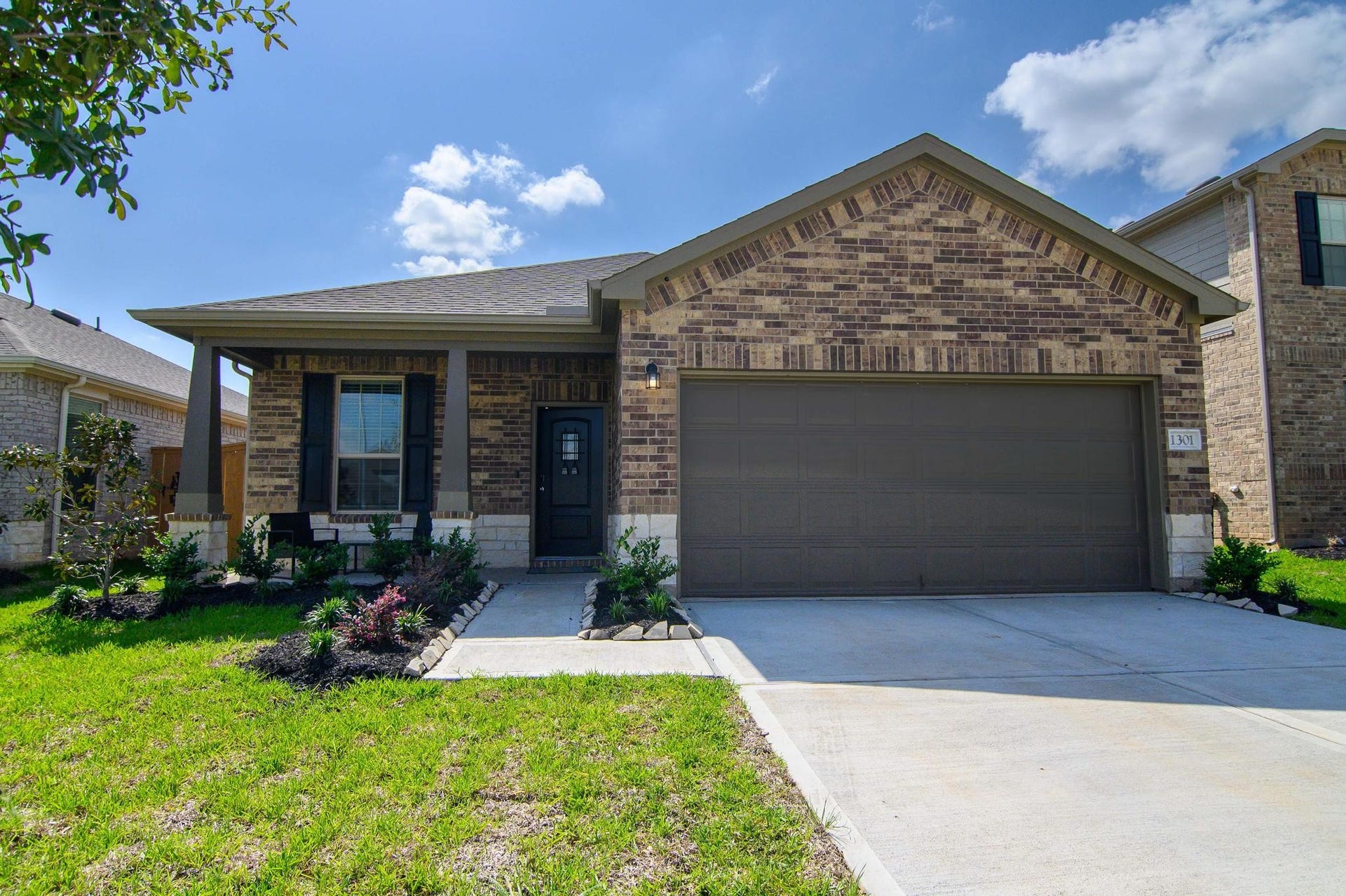 Charming single-story brick home with an inviting front porch, well-maintained landscaping, and a spacious two-car garage.