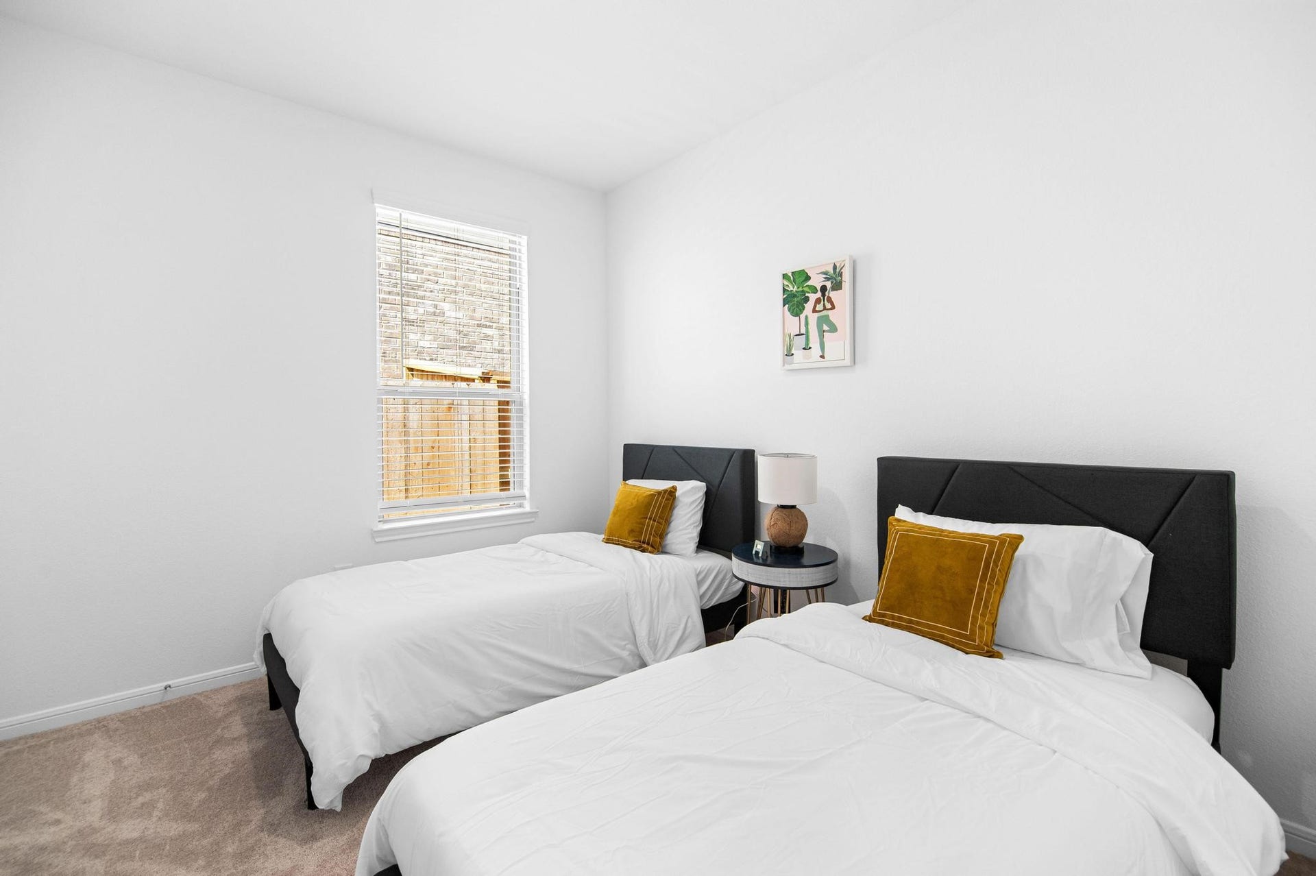 Bright and inviting bedroom featuring two twin beds with plush mustard accent pillows, complemented by a modern nightstand and soft carpeting.