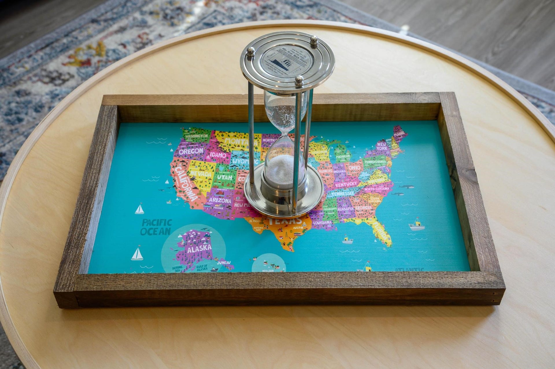 A stylish coffee table display features a colorful map of the United States framed in wood, complemented by an elegant hourglass centerpiece.
