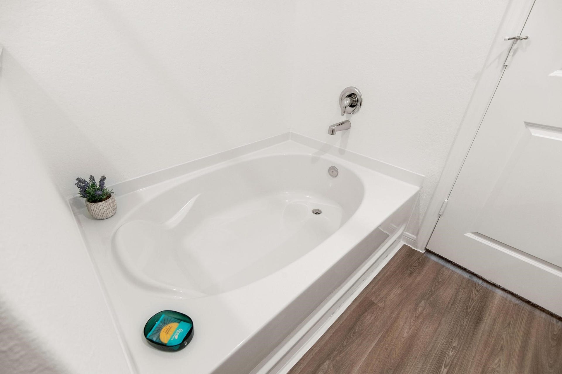 Modern bathroom featuring a sleek soaking tub with chrome fixtures, complemented by elegant wood-style flooring for a spa-like experience.
