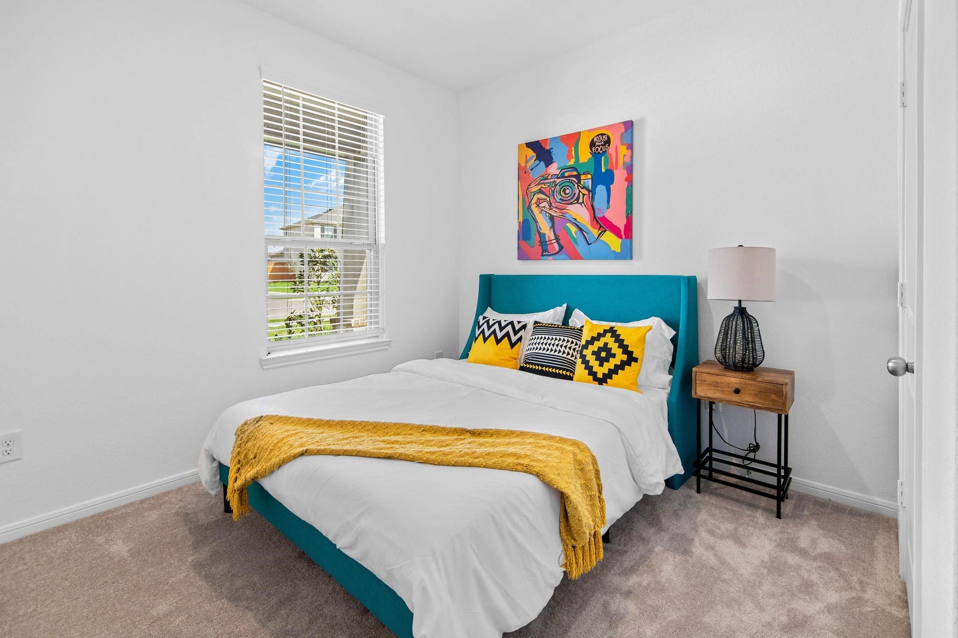 Bright and inviting bedroom with a colorful accent wall, cozy bed, and ample natural light from a large window.