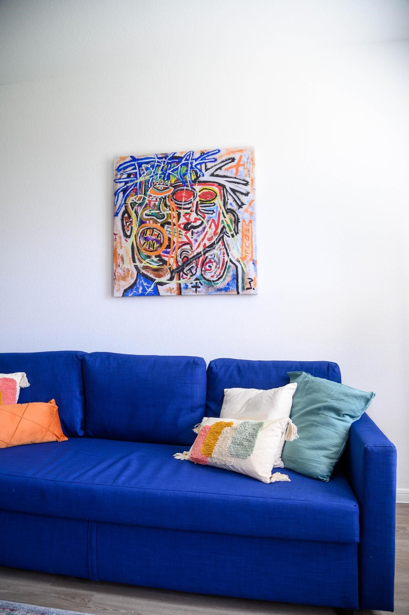 Vibrant living area featuring a bold blue sofa with colorful accent pillows, complemented by unique, eye-catching artwork on the wall.