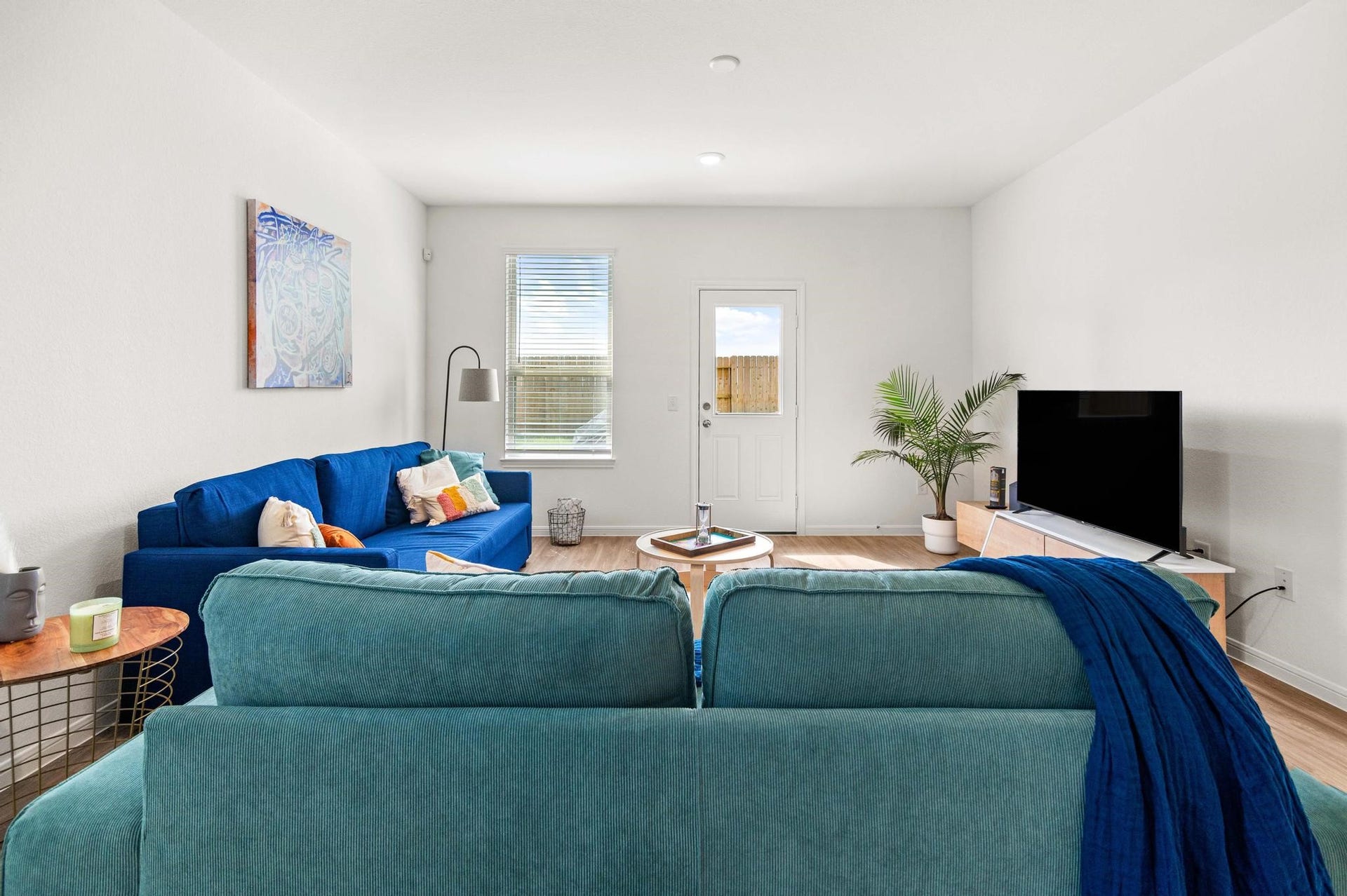 Bright and inviting living room featuring cozy blue sofas, a stylish coffee table, and a modern entertainment setup, all enhanced by natural light and a touch of greenery.