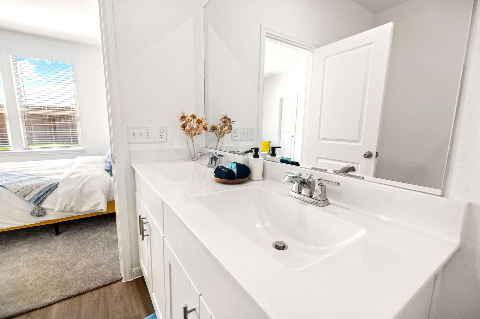 Elegant bathroom featuring a sleek double vanity with chrome fixtures, seamlessly connected to a cozy bedroom with abundant natural light.