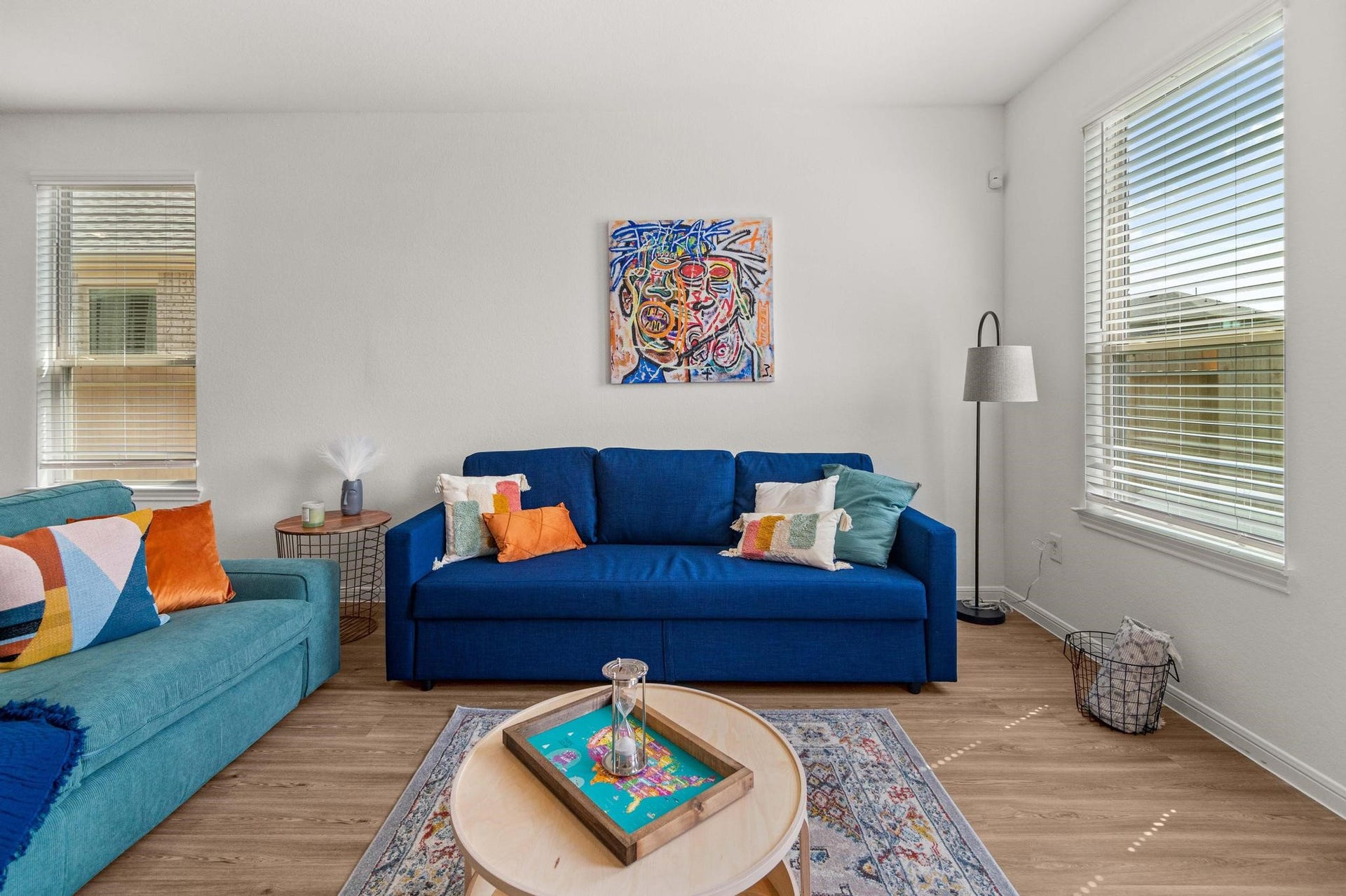 Bright and inviting living room with vibrant blue sofas, colorful cushions, and modern artwork, complemented by large windows that fill the space with natural light.