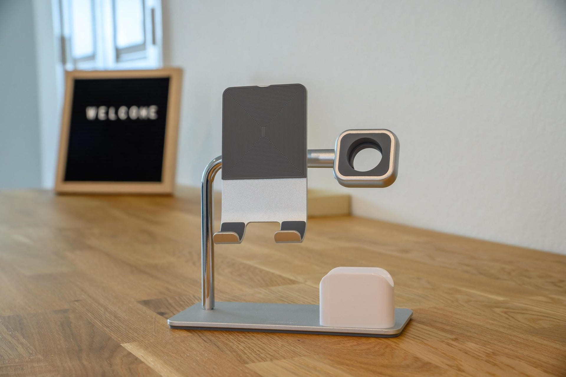 A modern, minimalist desk setup with a sleek wooden surface, complete with a stylish device stand and a welcoming sign, perfect for a home office.