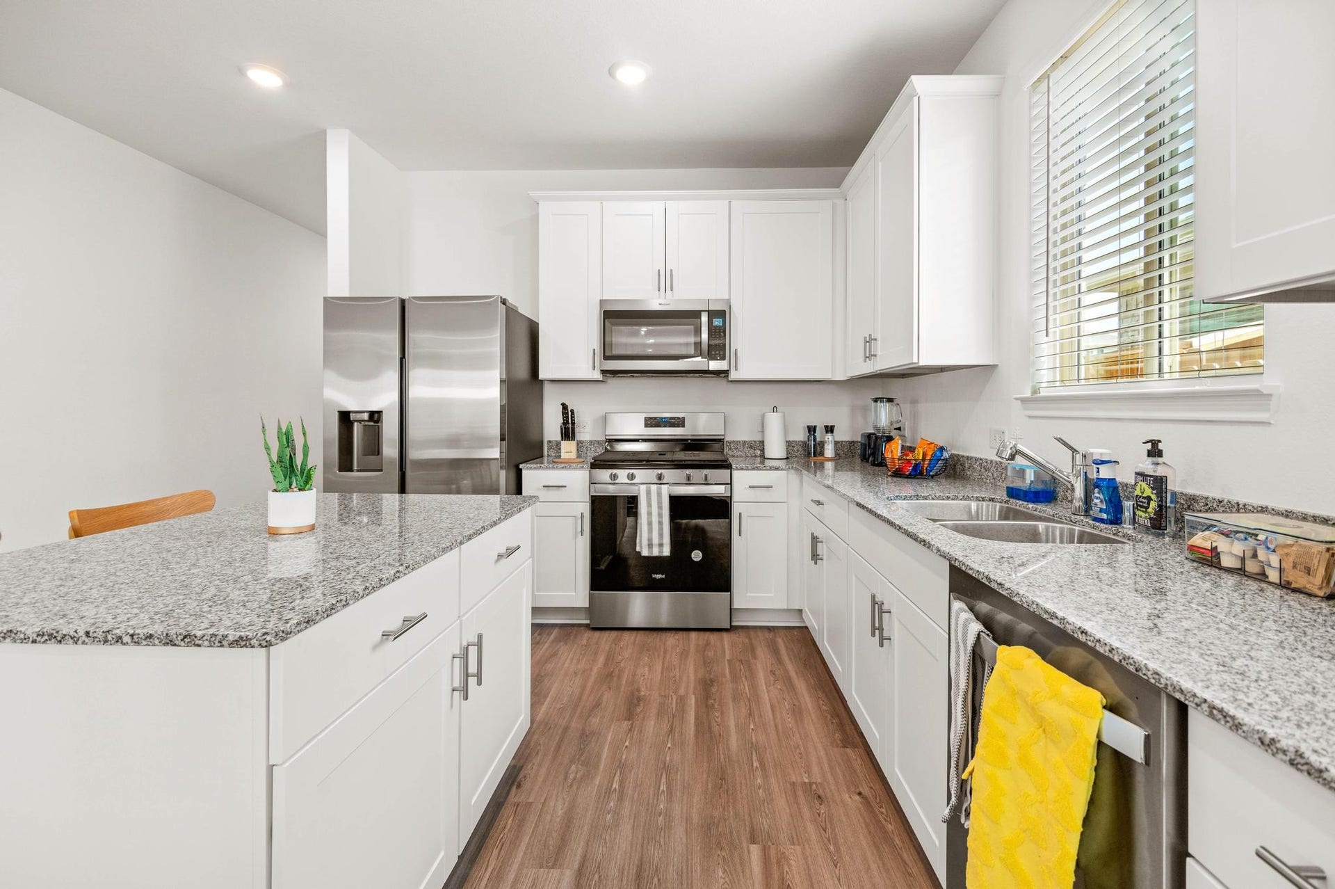 Modern kitchen with sleek stainless steel appliances, white cabinetry, and elegant granite countertops, complemented by warm wood flooring.